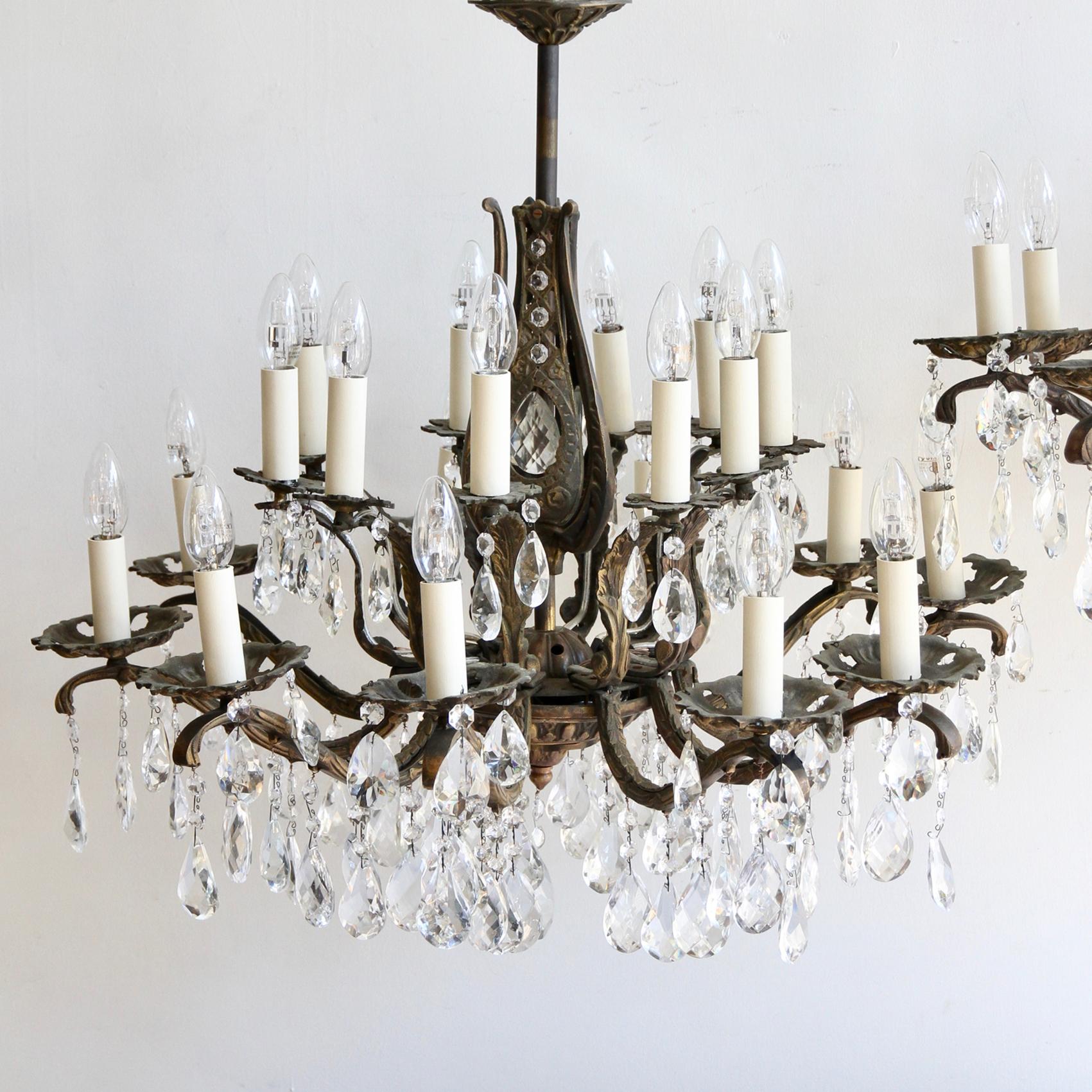 This pair of heavy cast ornate brass chandeliers originate from France, early 1900s and are dressed in a mix of fine cut glass harlequin drop and cut crystal pear drops. The chandelier frames are heavily oxidized each holding twenty lamps in total,