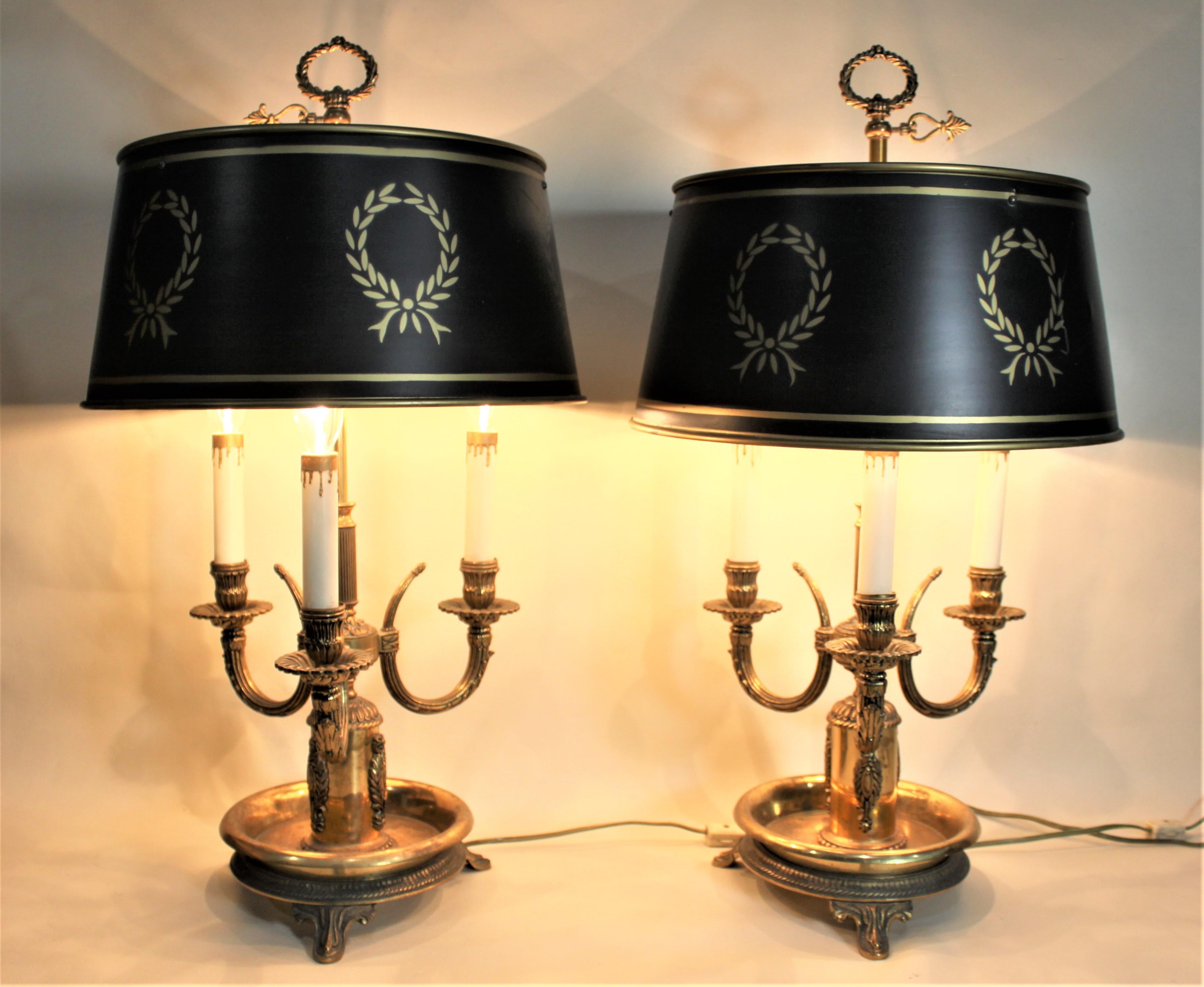 This matched pair of cast brass and tole painted shades were made in the mid-1960s in an antique French style, and most likely in the United States. Each lamp has a brass footed bowl with three candle styled lights and a tole painted black metal