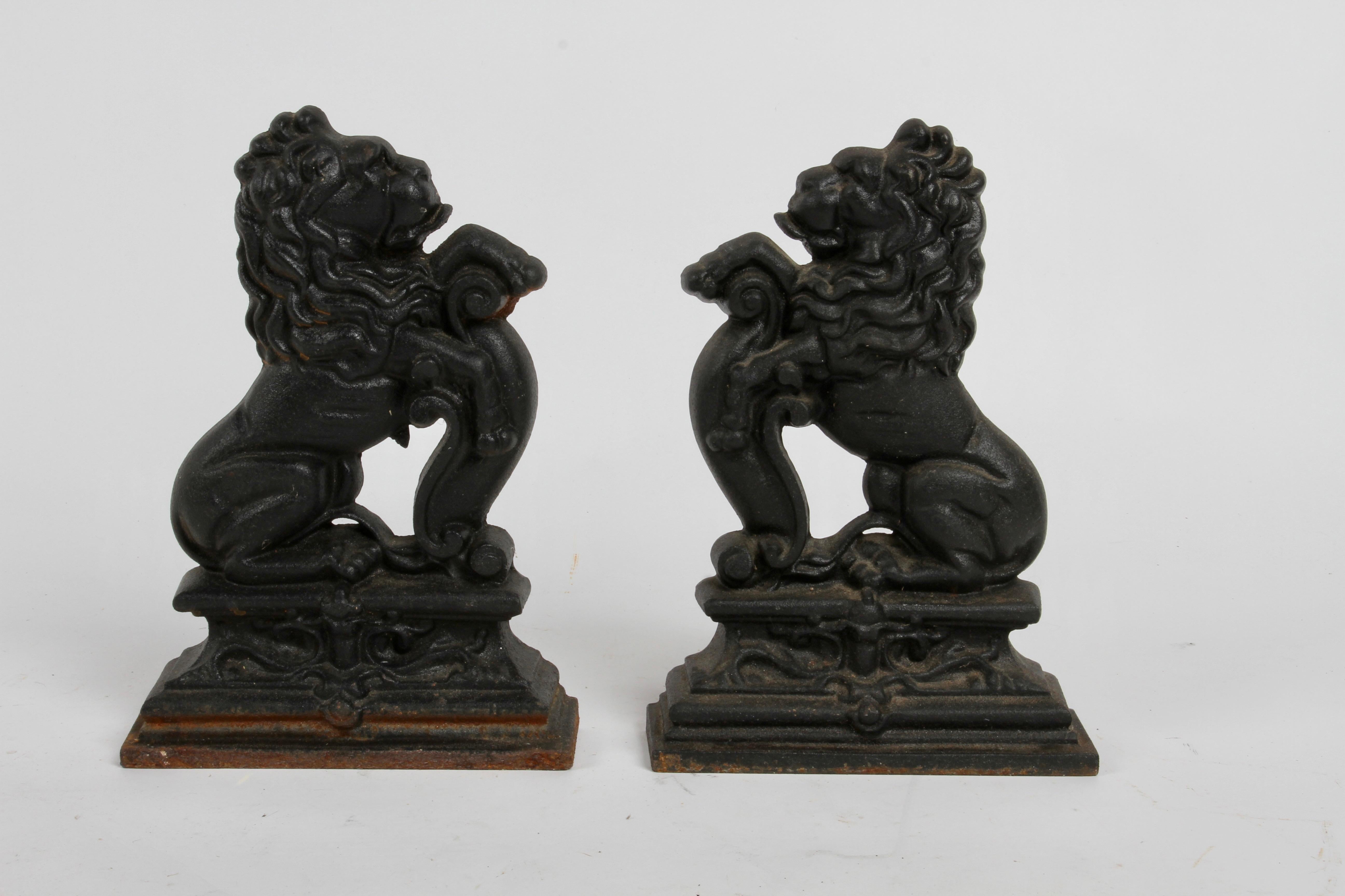 A wonderful pair of cast iron andirons or fire dogs, painted black and modeled as rampant lions standing on an integral plinth base. In the style of sculptor Alfred Stevens (1817-1875). Light rust to one of the bases, missing the iron log holders.