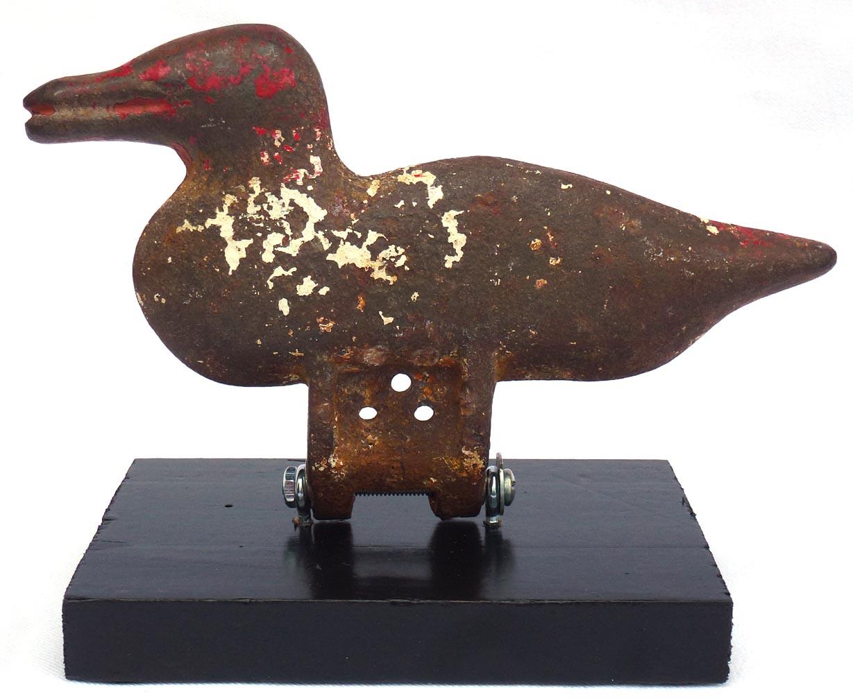 Here are two cast iron duck shooting gallery targets. They have dark oxidized surfaces with worn remnants of red and white paint. Each has been mounted on a wood display base. The ducks are 7 1/2
