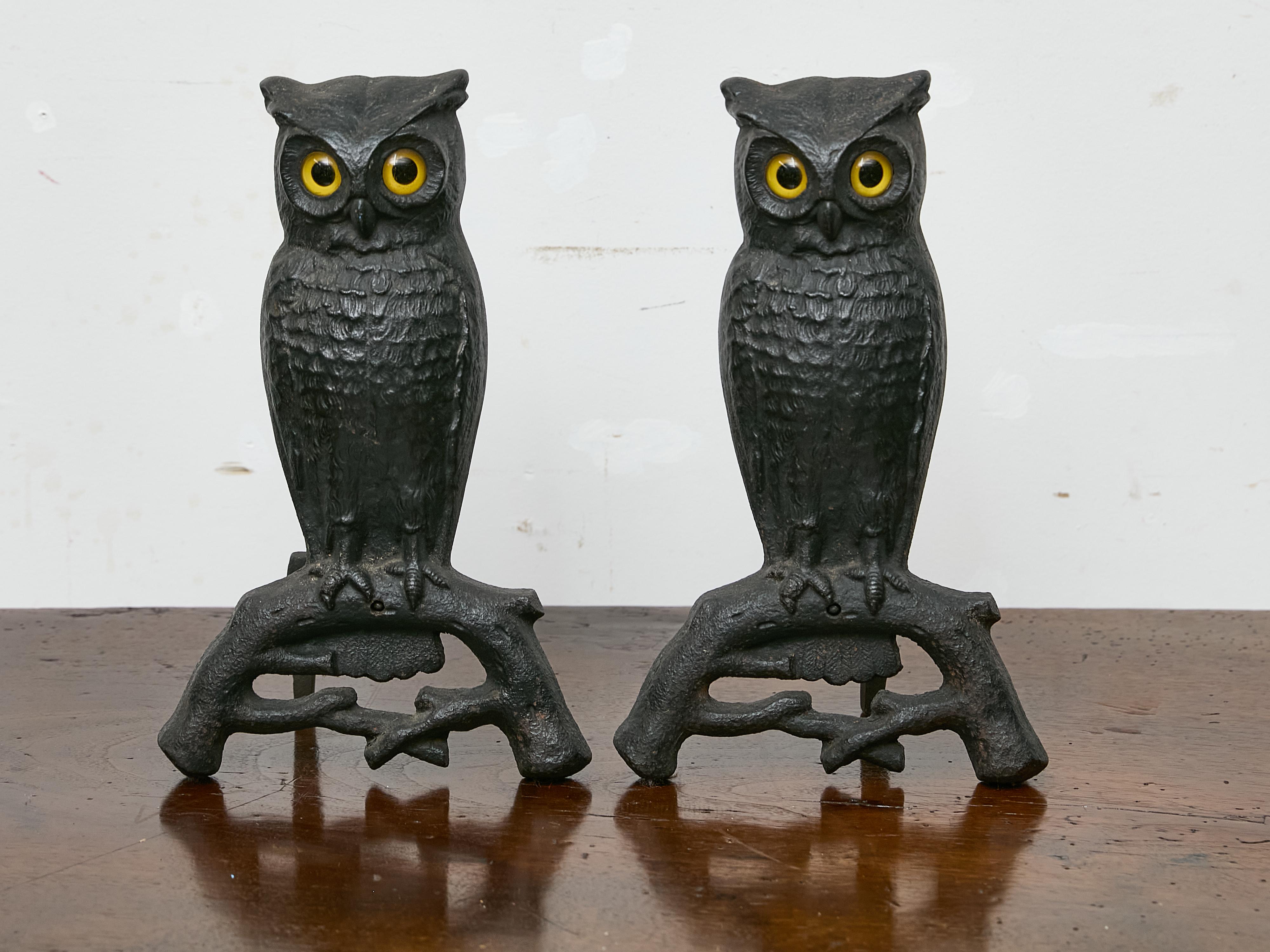 A charming pair of cast iron owl andirons from the United States, dating to the early 20th century, circa 1900. These whimsical fireplace accessories are cast in bold relief, depicting owls perched on stylized branches with their wings pressed