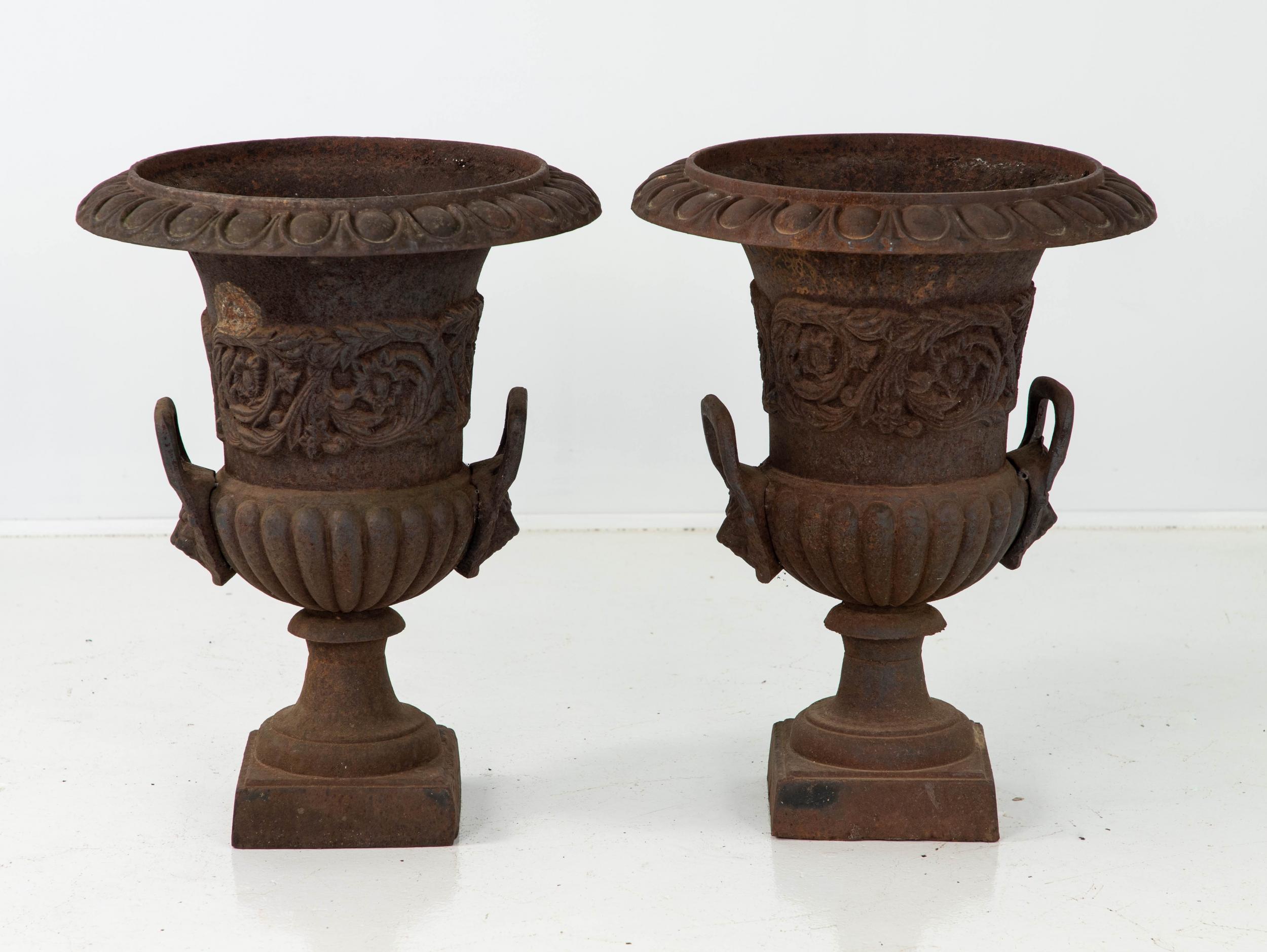 Pair of black painted cast iron urns. This pair features a floral band above the handles and an egg and dart pattern on the top rim. Some paint loss, rust spots, wear consistent with age and use.