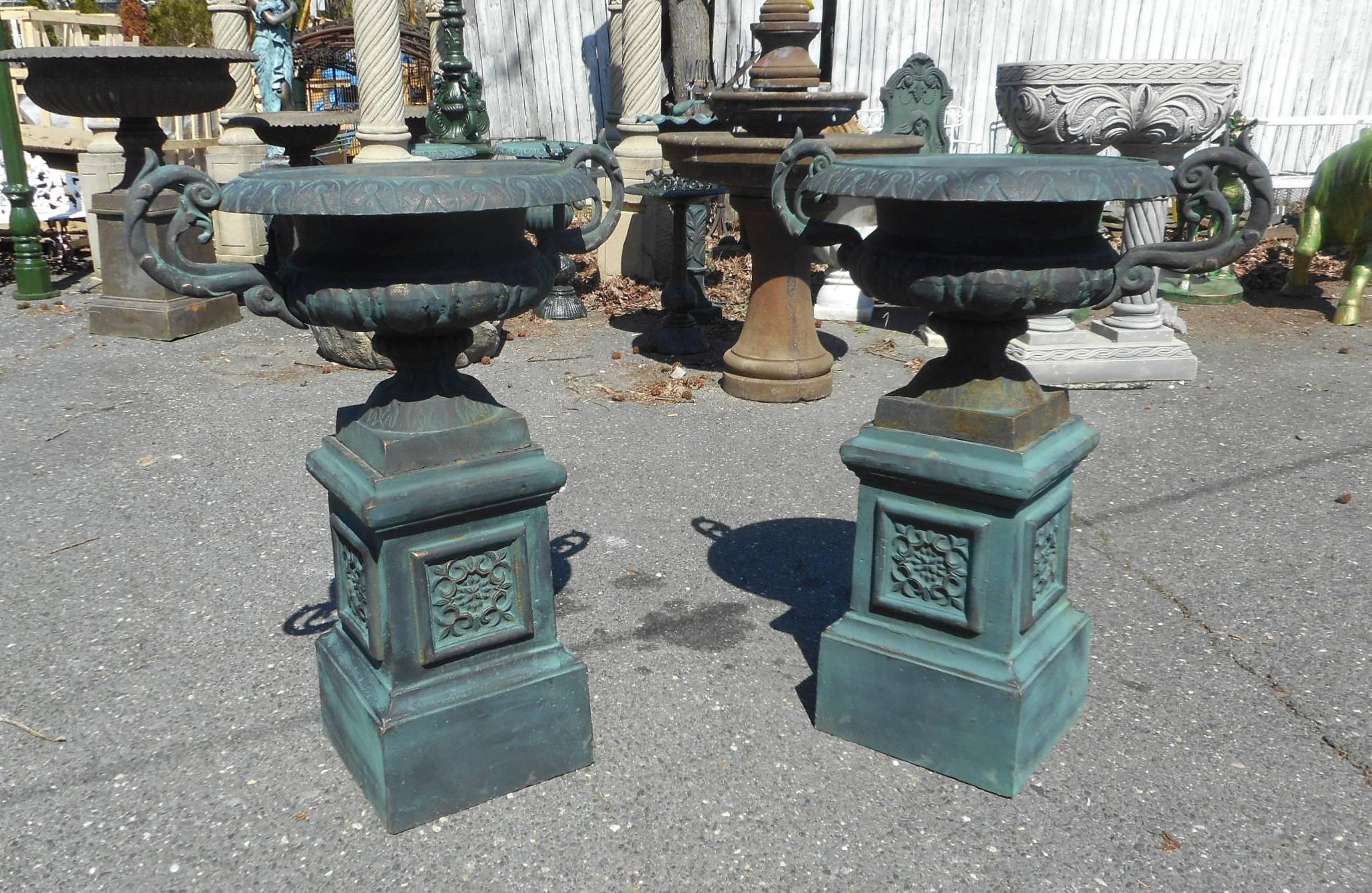 A stunning pair of cast iron urns sitting on top of a column base with unique designs. The wide opening on the top is perfect for a large floral arrangement. Fabulous scroll handle designs on each side of the top add to the allure. These wide mouth