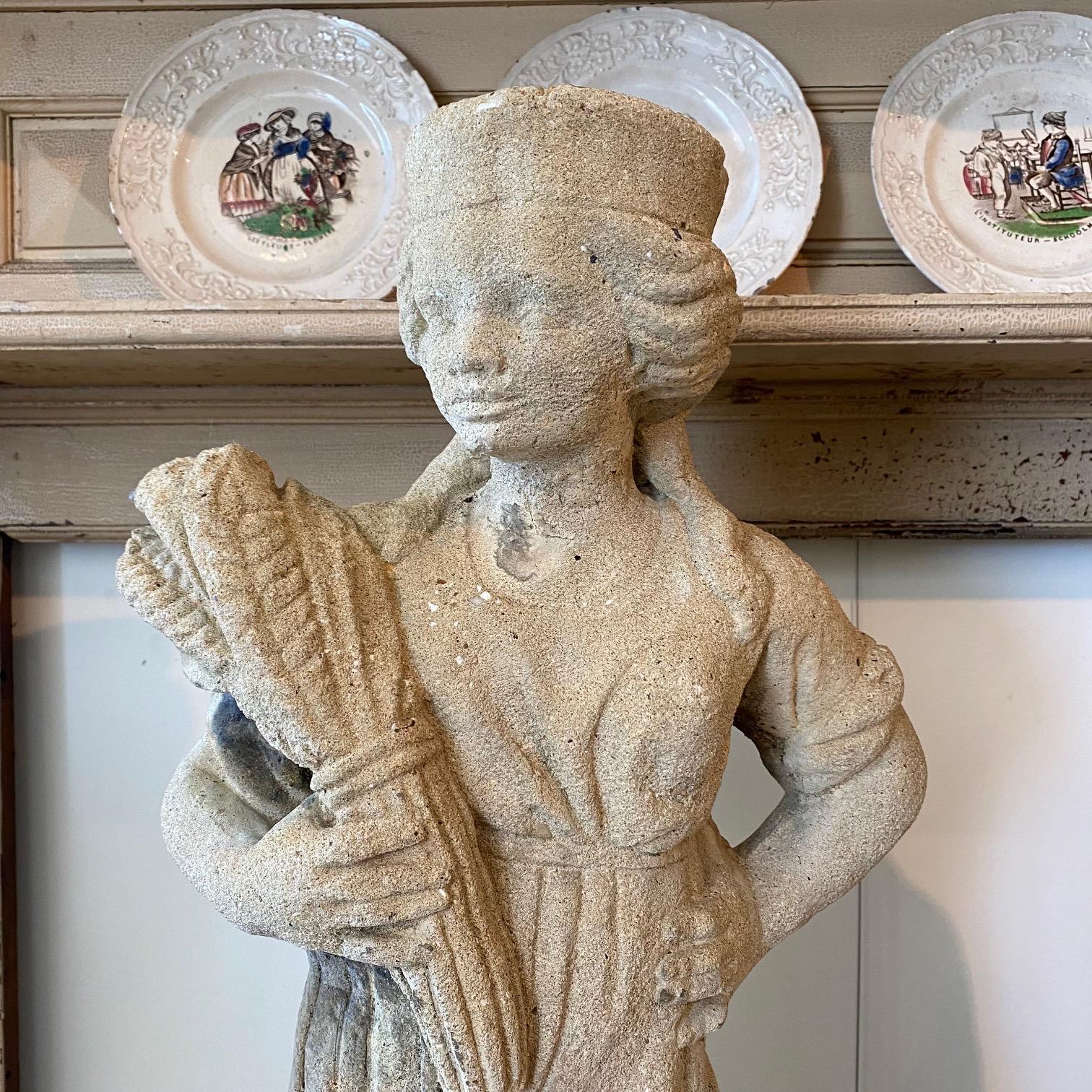 Really lovely pair of cast stone garden statues depicting a young woman or girl holding wheat sheaves and a young boy with asparagus or artichoke at his feet.  An outdoor accent for a garden or landscaping. Weathered patina. Would dress up any