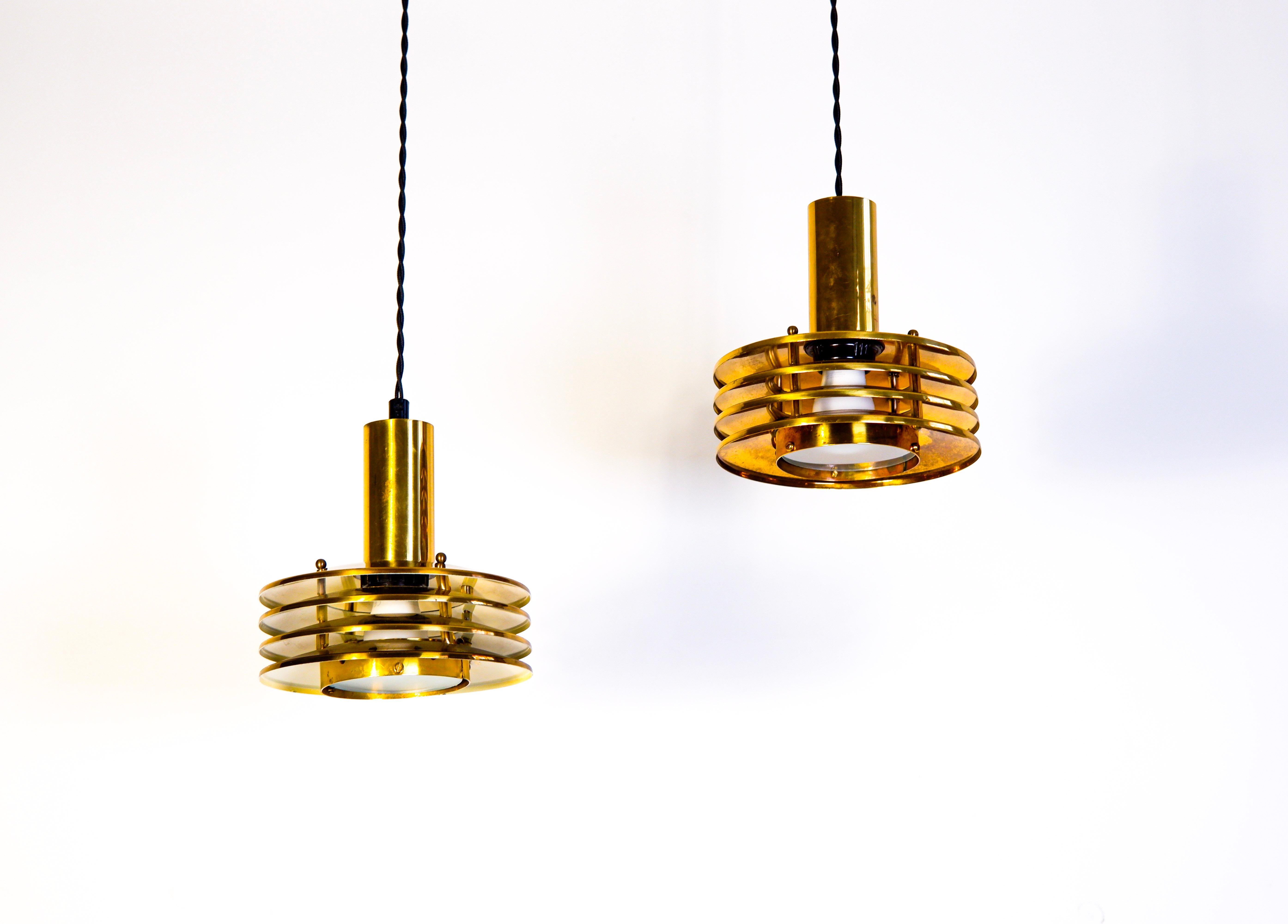 Rare paire de pendentifs attribuée à Kai Ruokonen ou à son frère Kari, en laiton massif avec 4 anneaux et un diffuseur en verre. L'état général est bon et les lampes ont une bonne patine avec des traces d'utilisation et d'âge. La lampe est composée