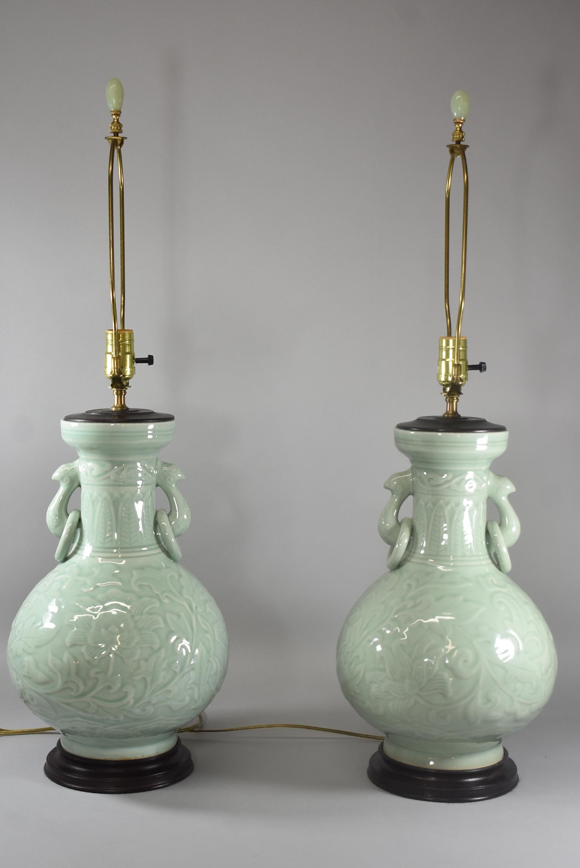 Pair of sea-foam green antique Celadon porcelain Asian lamps. The lamps feature a stunning celadon finish over subtle floral detailing. Mid-20th century urn style, ring handles, wooden bases, single socket, and 3-way switches. Measures: 30 1/2