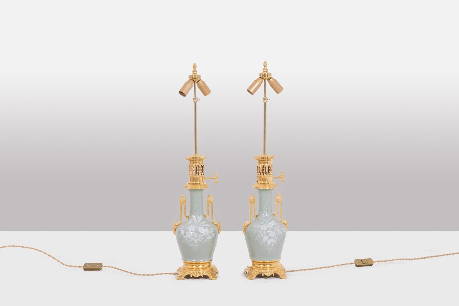 Pair of baluster-shaped Celadon porcelain and gilded bronze lamps, the porcelain decorated with white flowers. Quadripod base decorated with motifs, top of the frame decorated with an openwork gallery and a key. Finely decorated handles.

French