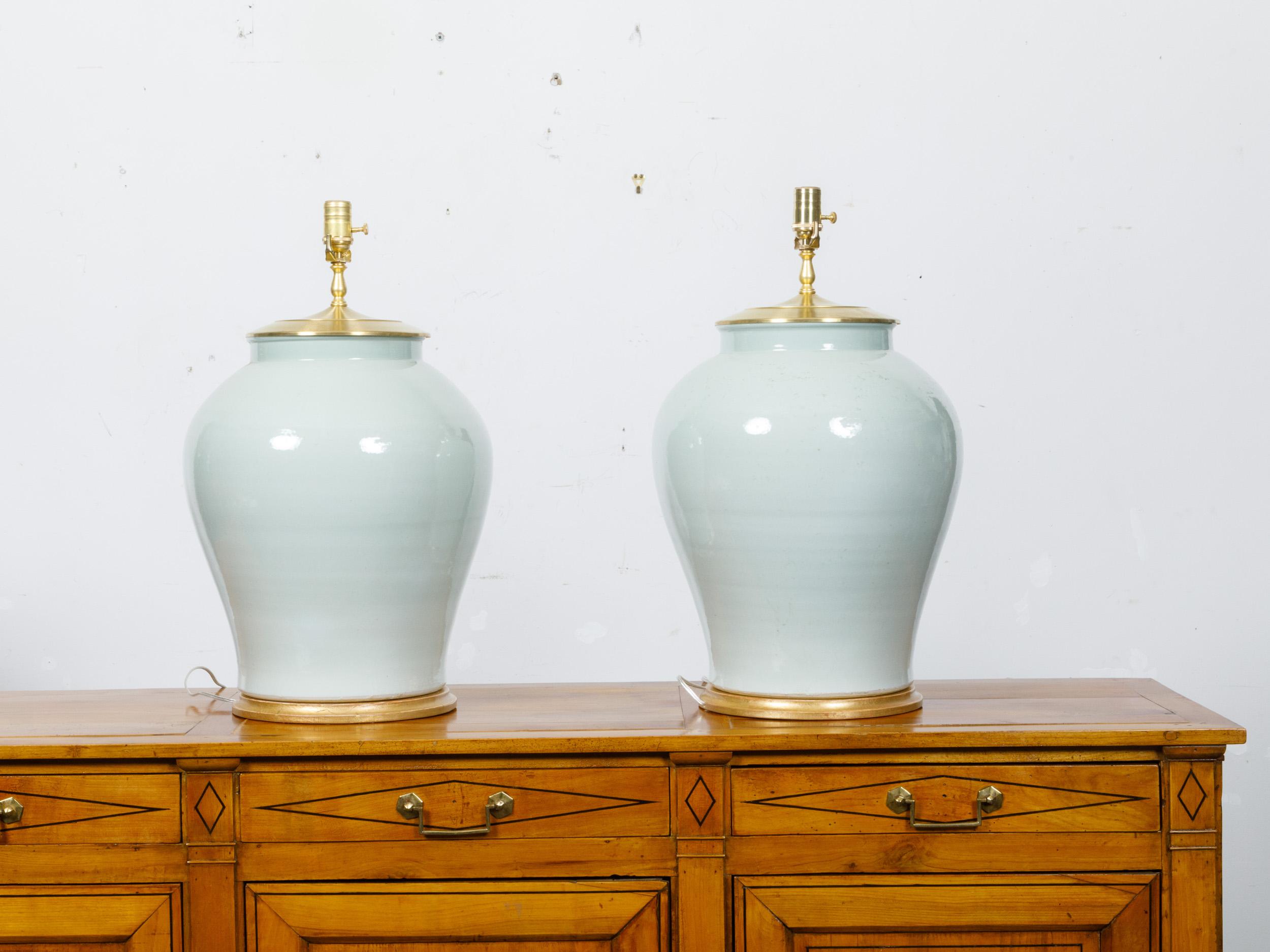 A pair of celadon porcelain table lamps mounted on circular giltwood bases and wired for the USA. This pair of elegant table lamps, crafted from celadon porcelain, features a soft, serene green glaze that embodies the timeless grace of traditional