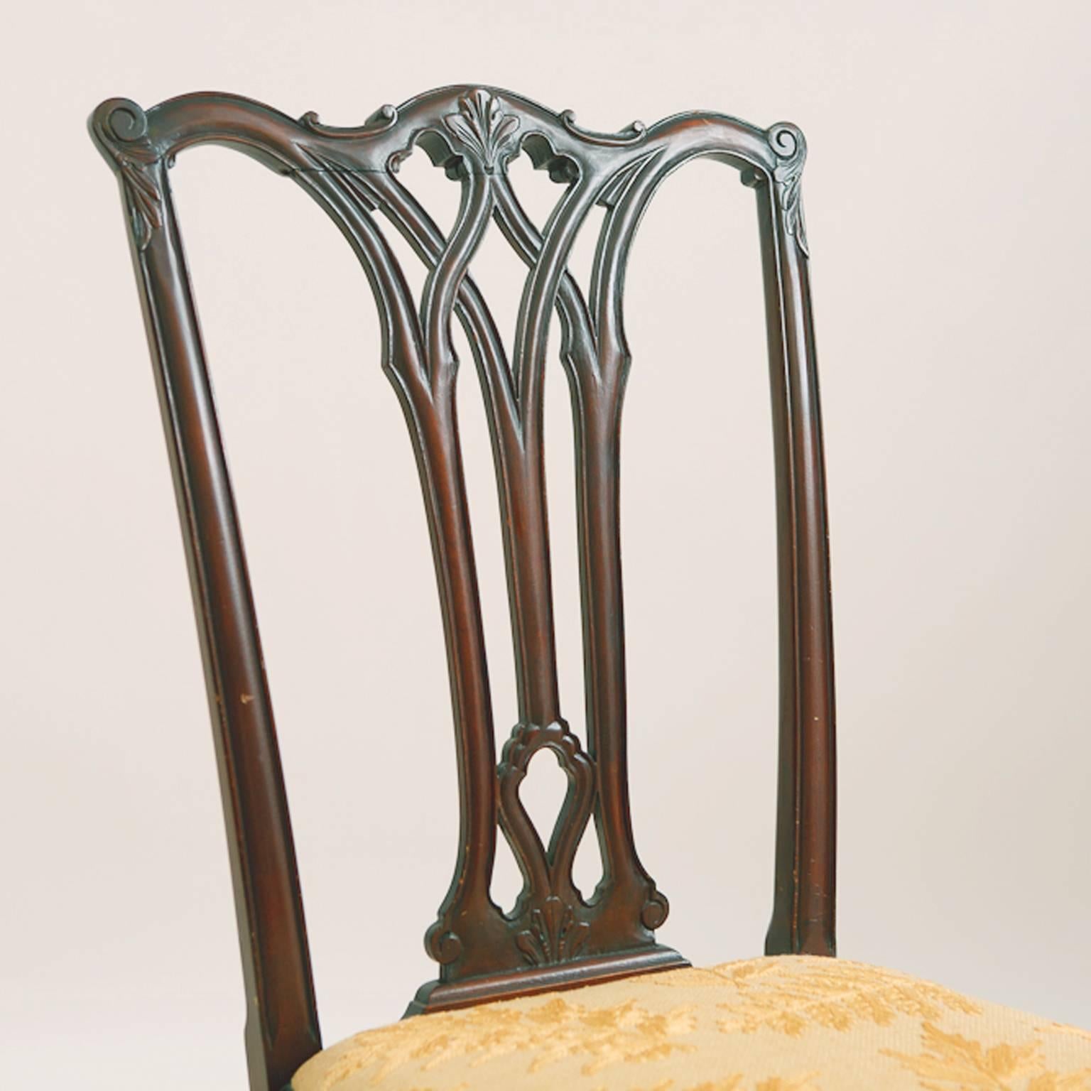 Coppia di sedie da pranzo in stile Chippendale con schienali a stecca forati, fregi anteriori della seduta montati a conchiglia e piedi anteriori a sfera. I sedili a slitta sono stati rivestiti di recente con un antico tessuto color oro con ricami a