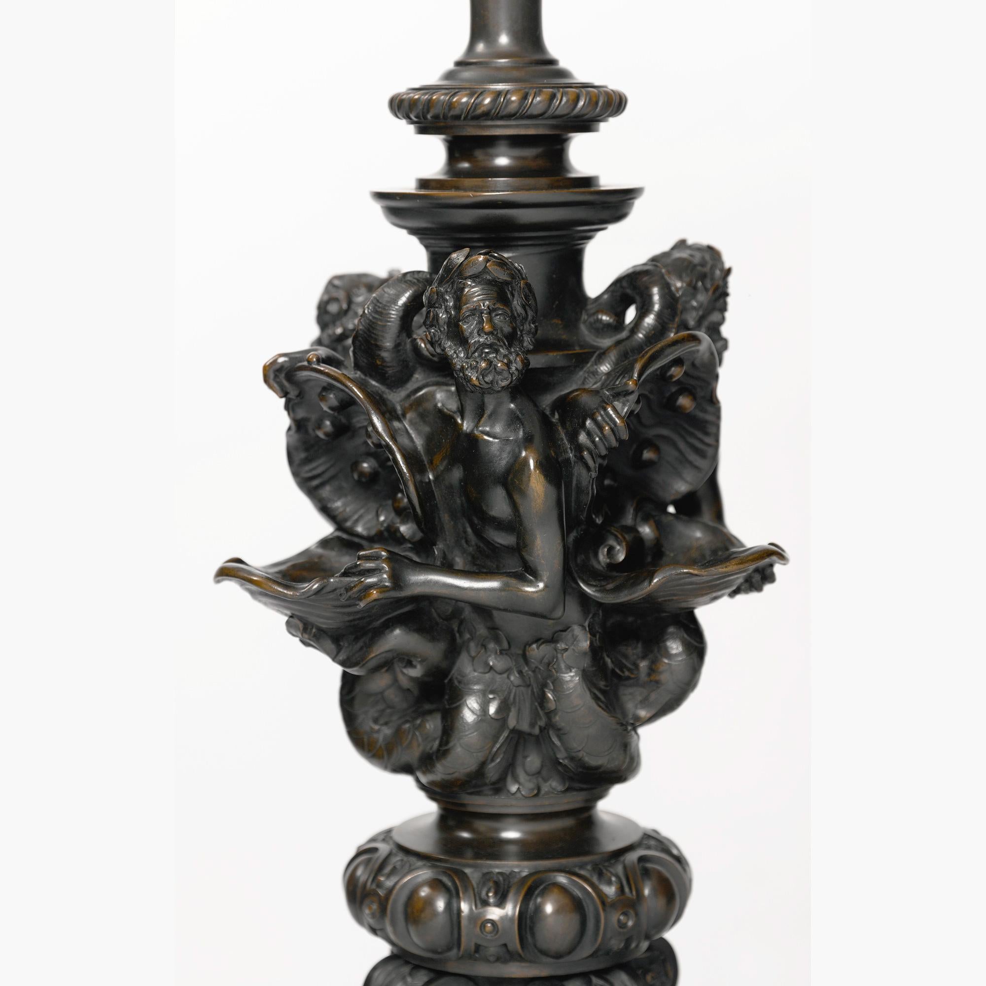 A pair of 19th century Néo-Renaissance carved marble and patinated bronze floor lamps each bronze stem cast with three Tritons holding conch shells, the tri-partite base with putti riding dolphins and chimères to each bottom corner, the carved
