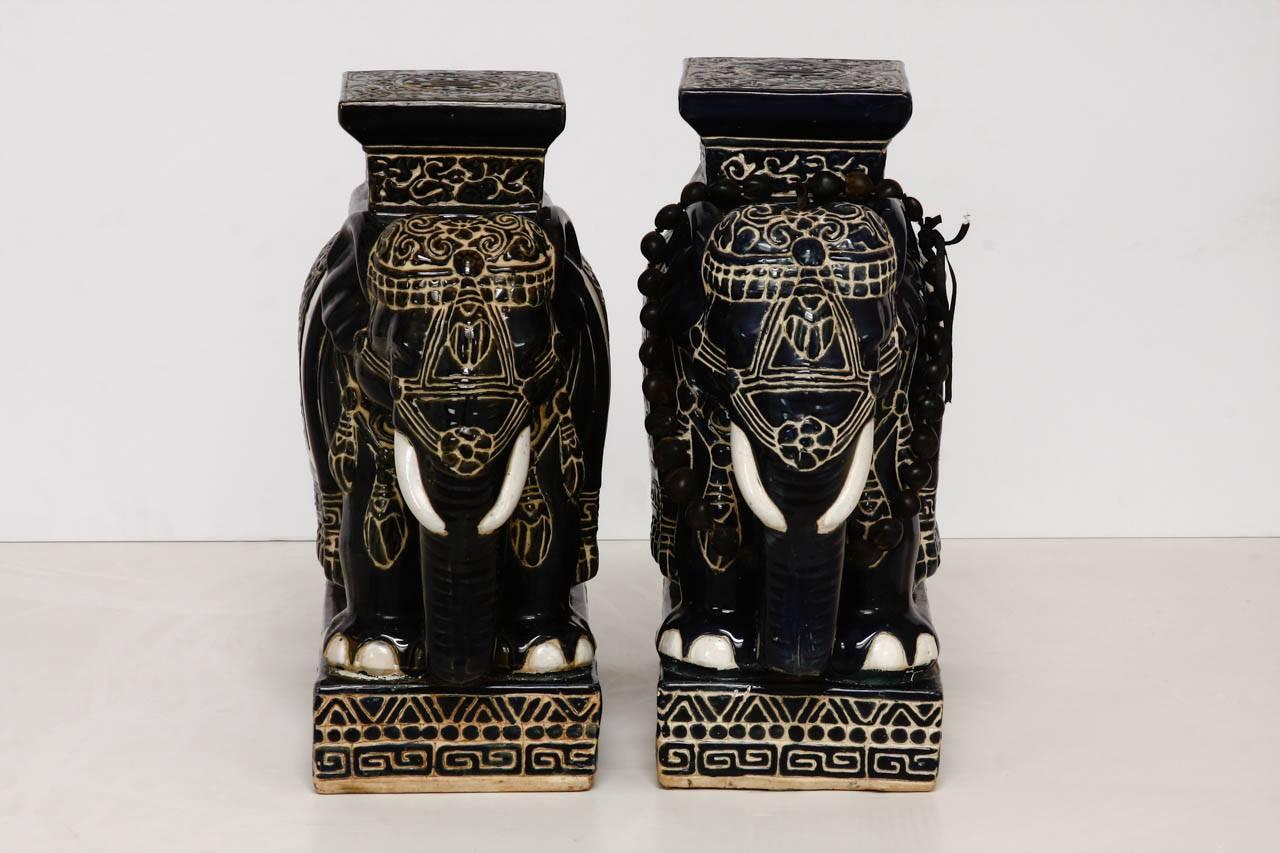 Rare pair of navy blue glazed ceramic elephant garden stools or drink tables. Featuring an amazingly dark blue finish that accents the caparisoned bodies, and bases which have a Greek key motif border. Very good condition with no losses and minor