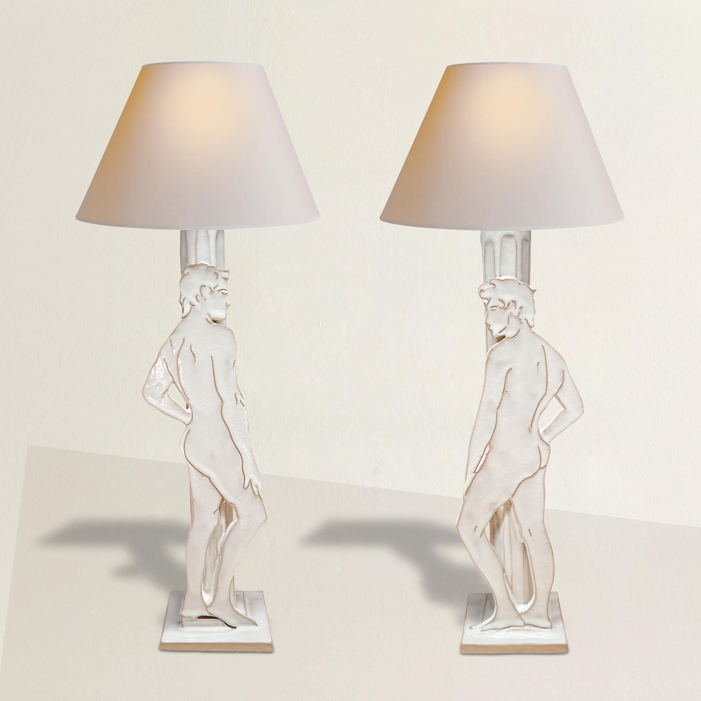 A stunning and chic pair of 21st century Brazilian artist-made glazed hand-built ceramic table lamps each with a unique hand-drawn male nude figure in contrapposto and leaning against a fluted column. Wired for US with white paper shades.