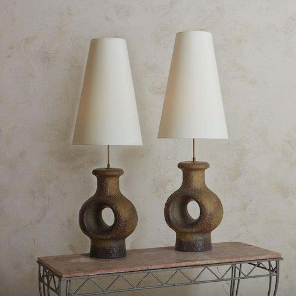 A pair of 1960s Danish table lamps designed by Travail Danois for Belysning in the 1960s. These large-scale brutalist stoneware ceramic lamps have a sculptural base with a circular cutout detail. They feature a textured, porous finish and a range of