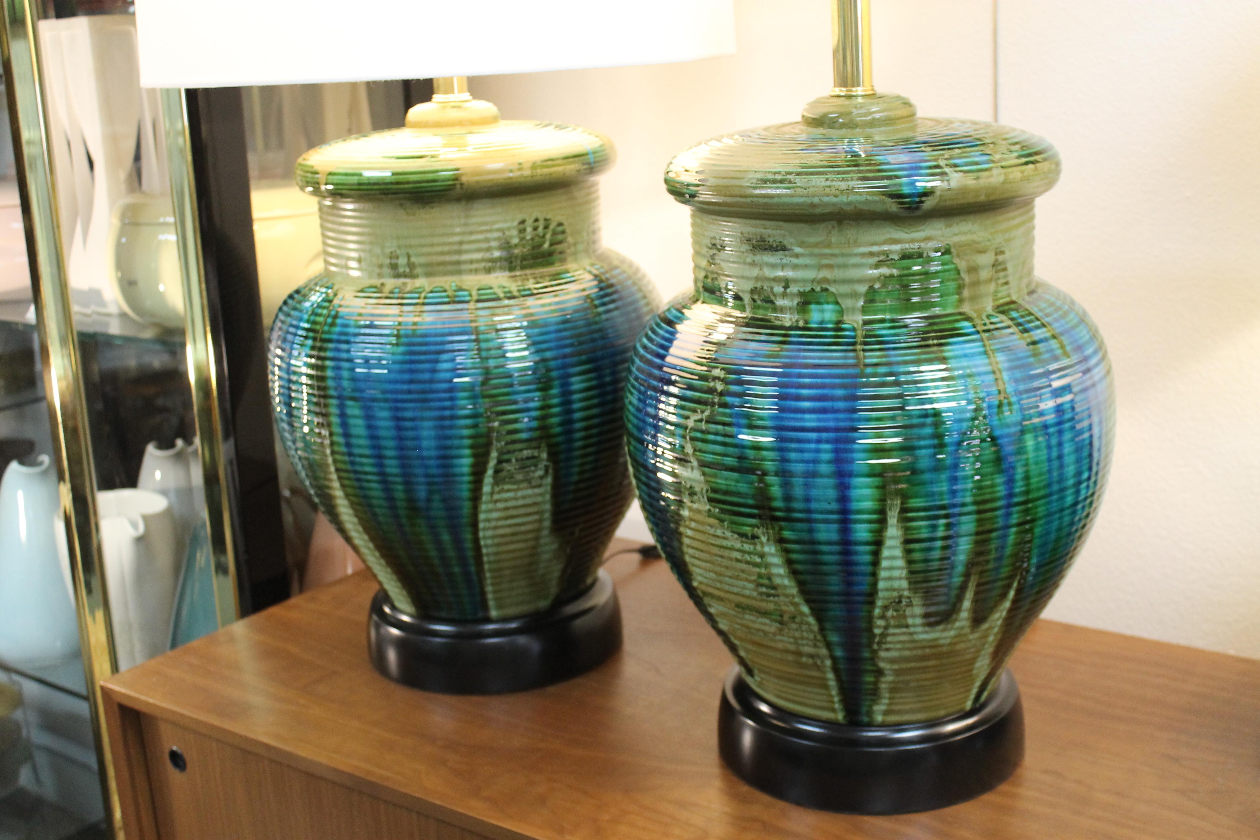 Monumental pair of ceramic lamps. Pottery lamps have abstract patterns of greens, blues, yellows. Lamps have been professionally rewired for a 3 way light bulb. Lamps measure 24.5