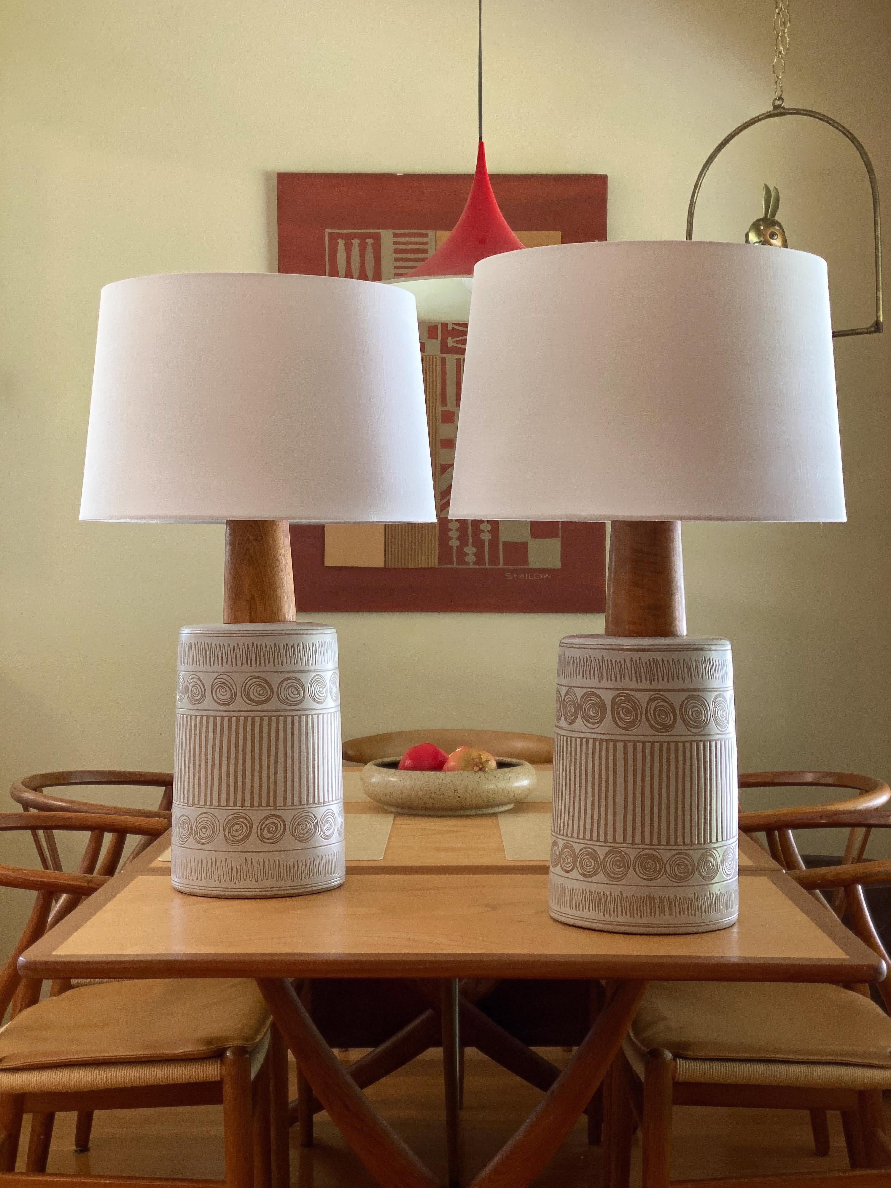 Pair of elegant table lamps by ceramicist duo Jane and Gordon Martz for Marshall Studios. Features wonderful sgraffito decorations on a flat white glazed body. Details are outstanding, walnut neck and finials and brand new shades.

Overall
