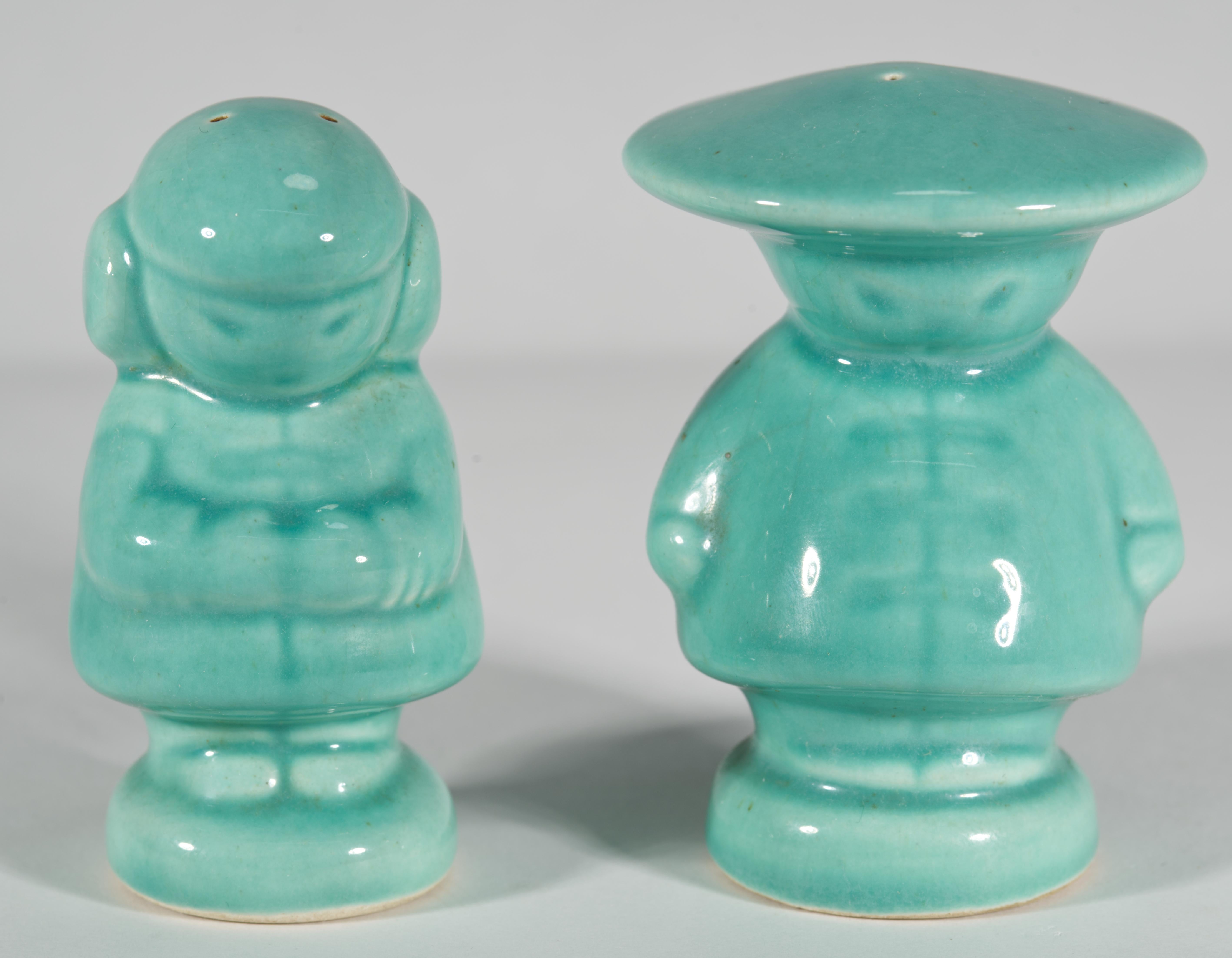 Ein Paar charmanter Salz- und Pfefferstreuer im Vintage-Stil zeigt einen Jungen und ein Mädchen in traditionellen asiatischen Kostümen; die Streuer sind mit Seladonglasur verziert. Die Wahl einer einfarbigen Palette unterstreicht die skulpturalen,