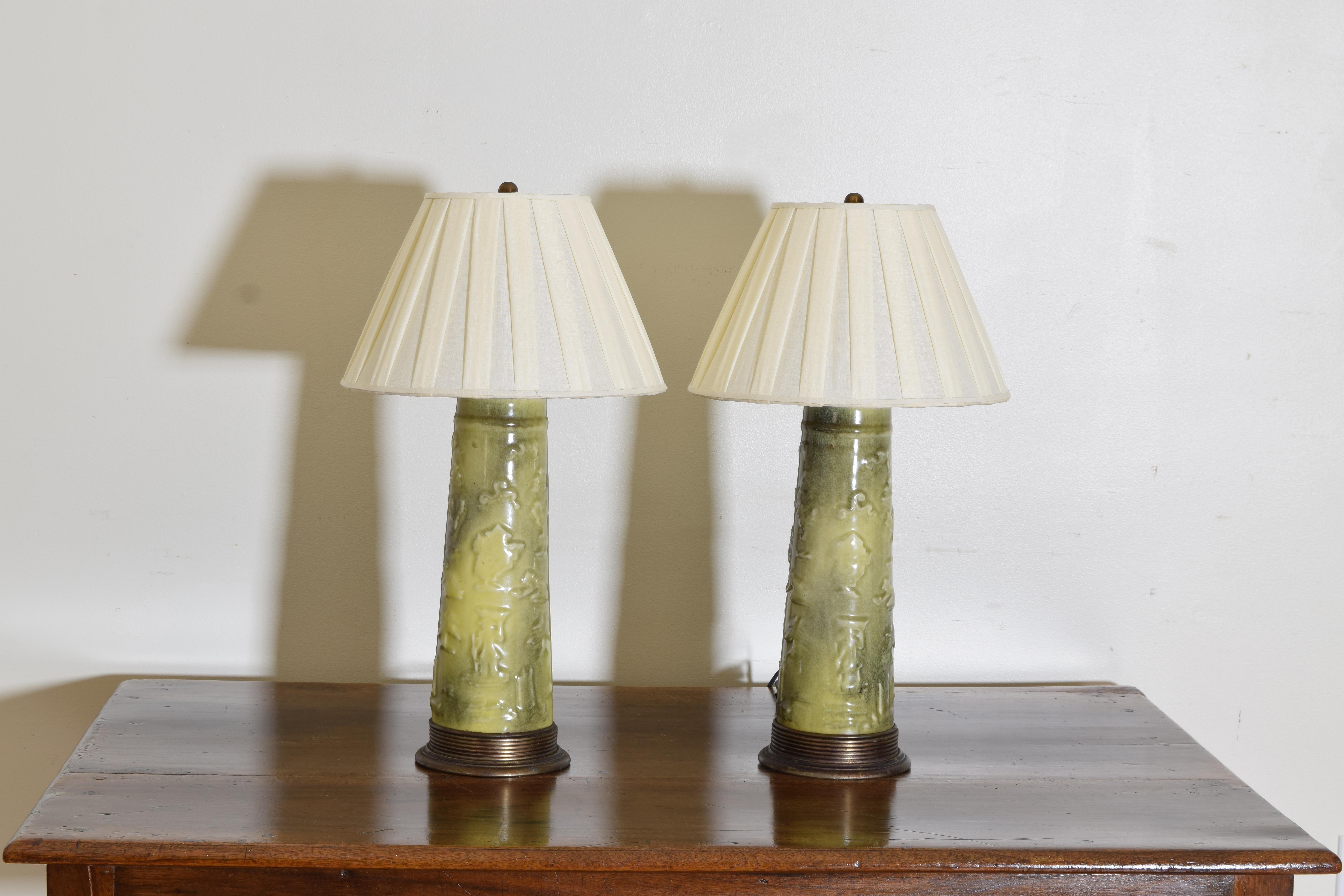 Cast ceramic lamps with raised foliage and figurative designs mounted on tapered brass bases with brass tops