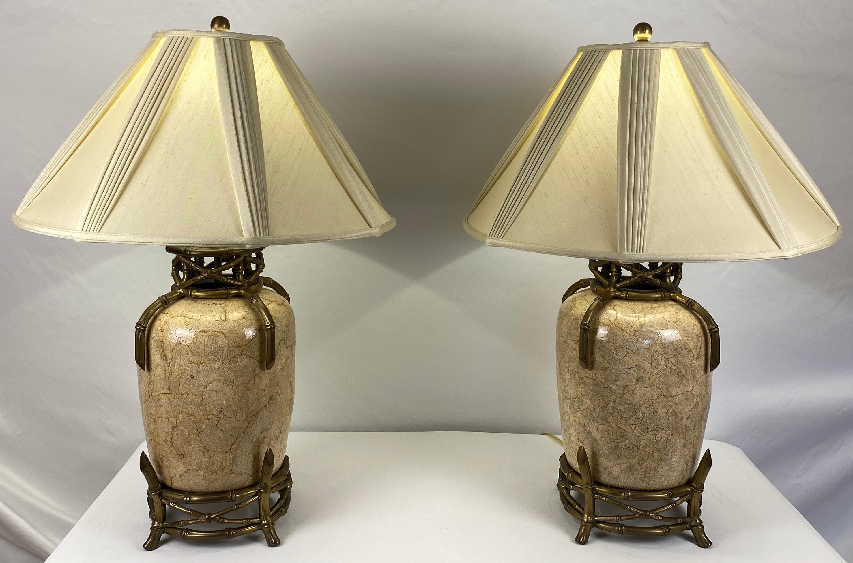 A very stylish pair of table lamps composed of ceramic and brass with faux bamboo accents including large custom made beige silk blend lamp shades. This handsome pair of beige table lamps are very versatile due to their neutral earth tones. Fine