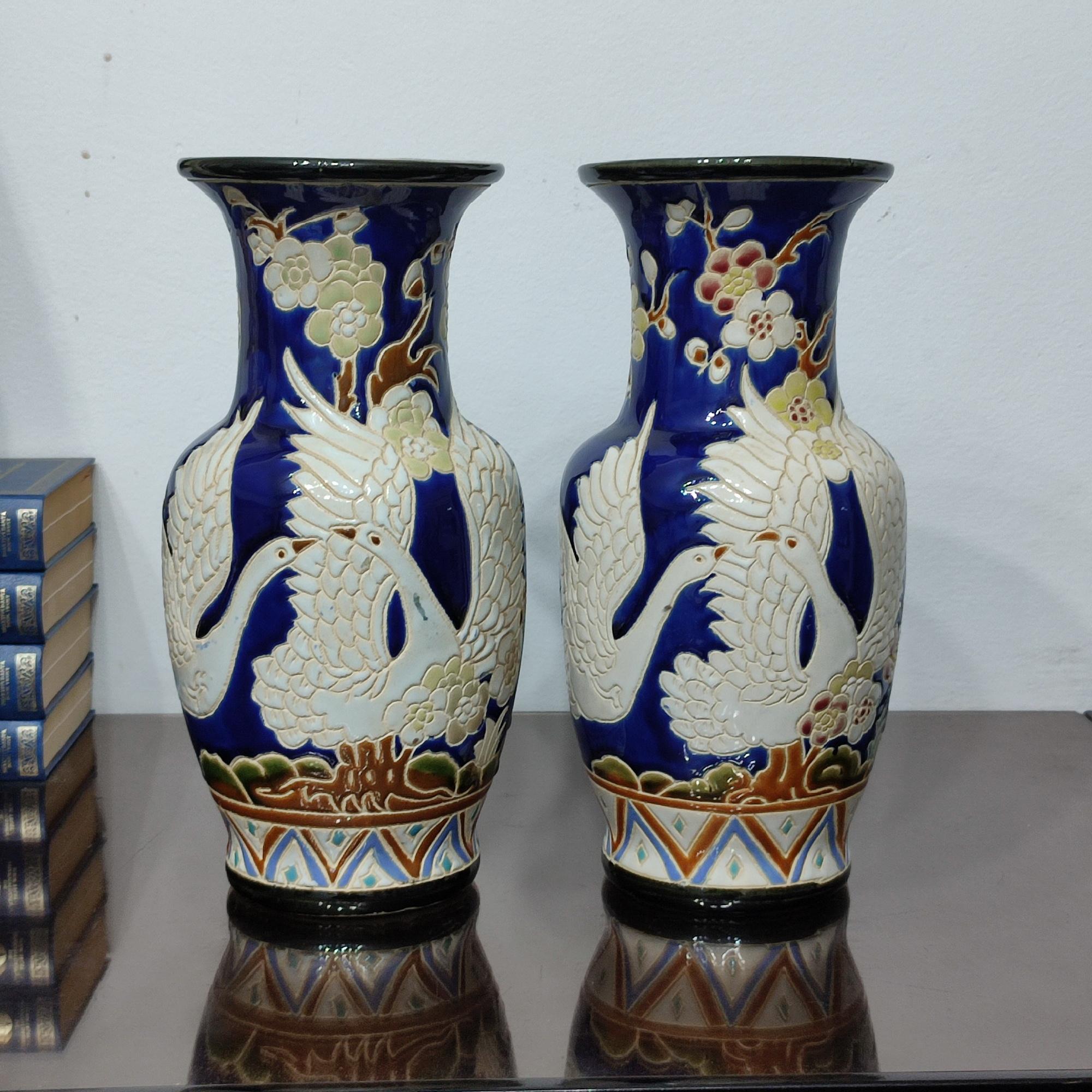 Amazing pair of Scandinavian pottery vases, decorated all around with flying swans, richly decorated with colorful glaze, cherry flowers and branches against a royal blue background, with oriental influence. Atelier pieces, hand marks on the