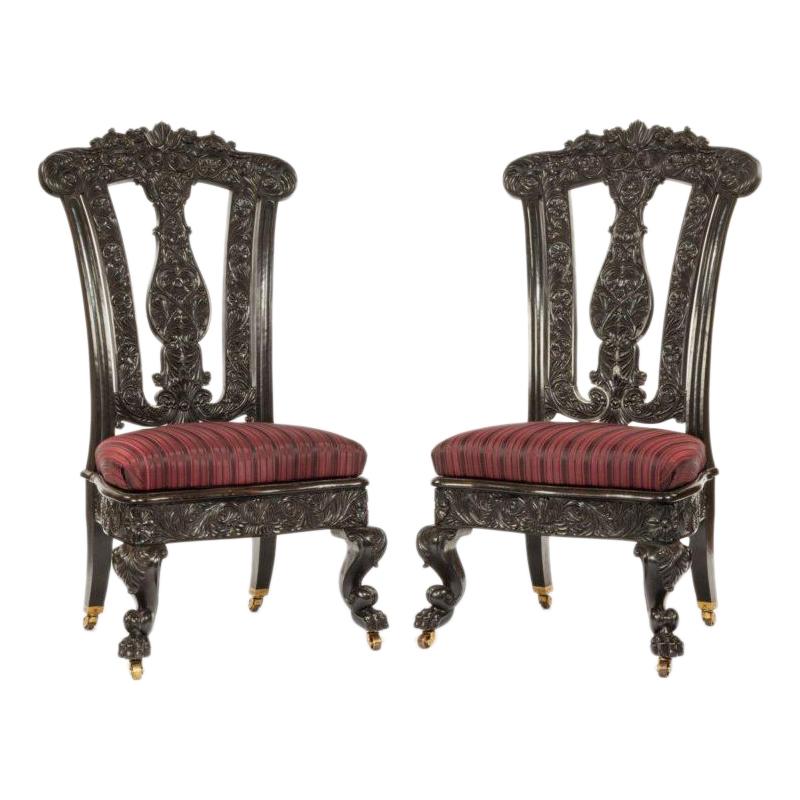 A pair of Ceylonese solid ebony hall chairs each with a baluster splat, upholstered seat and scrolling cabriole front legs, boldly carved with floral arabesques, fleshy acanthus leaves and palmettes, caster wheels replaced, circa 1850.

Measures: