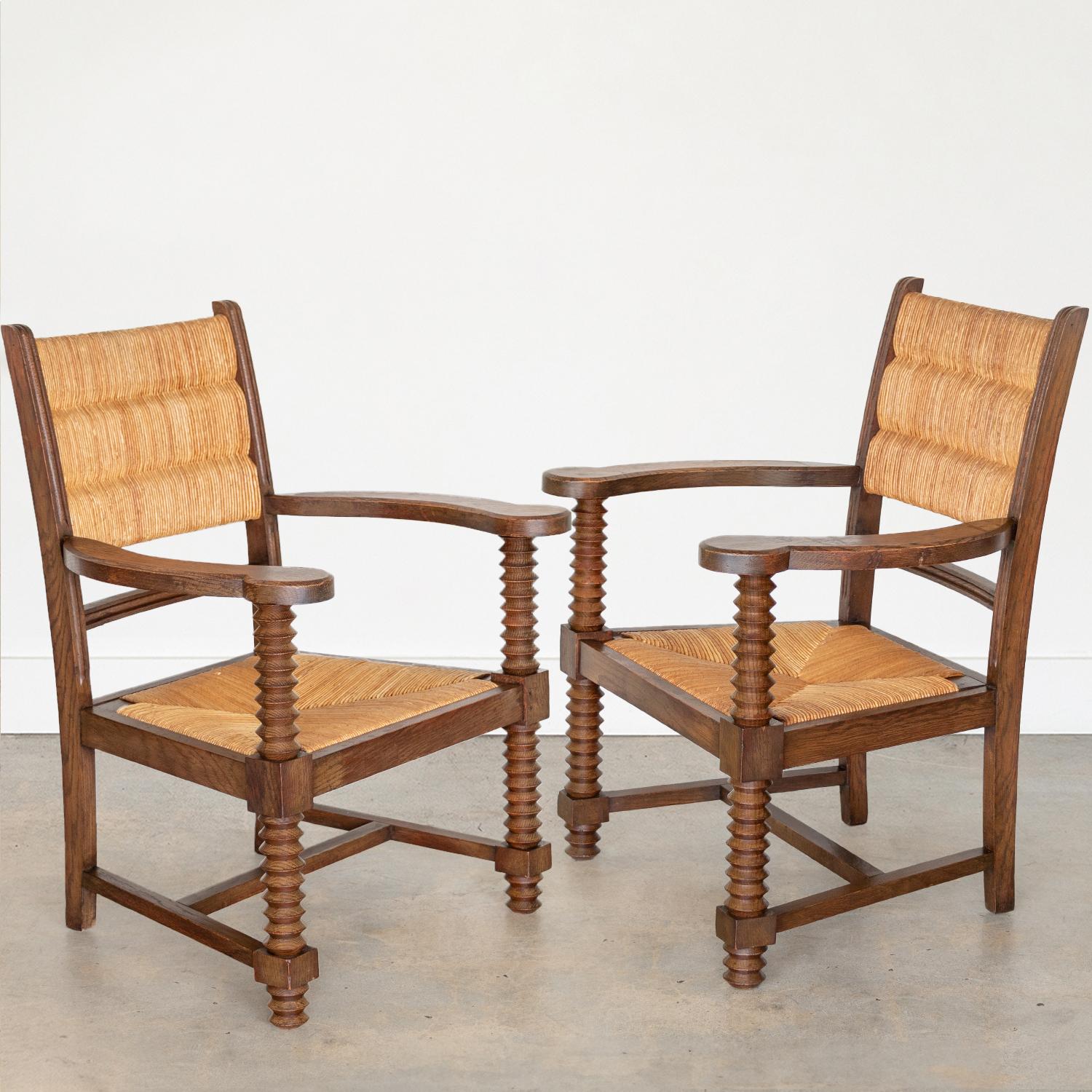 Great pair of carved wood armchairs by Charles Dudouyt from France, 1940s. Beautiful woven rush back and seat. Intricate carved wood detail on arms, legs, and wood frame with dark stain. Sold as a pair.