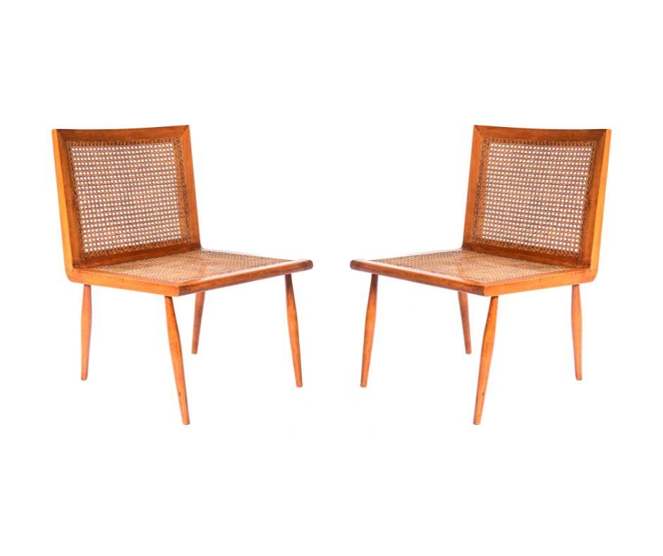 Delicata e raffinata, questa coppia di poltroncine da letto esemplifica l'esplorazione di Joaquim Tenreiro della struttura e della leggerezza. Realizzate in legno di peroba do campo con sedute e schienali in canna, la loro geometria sobria è