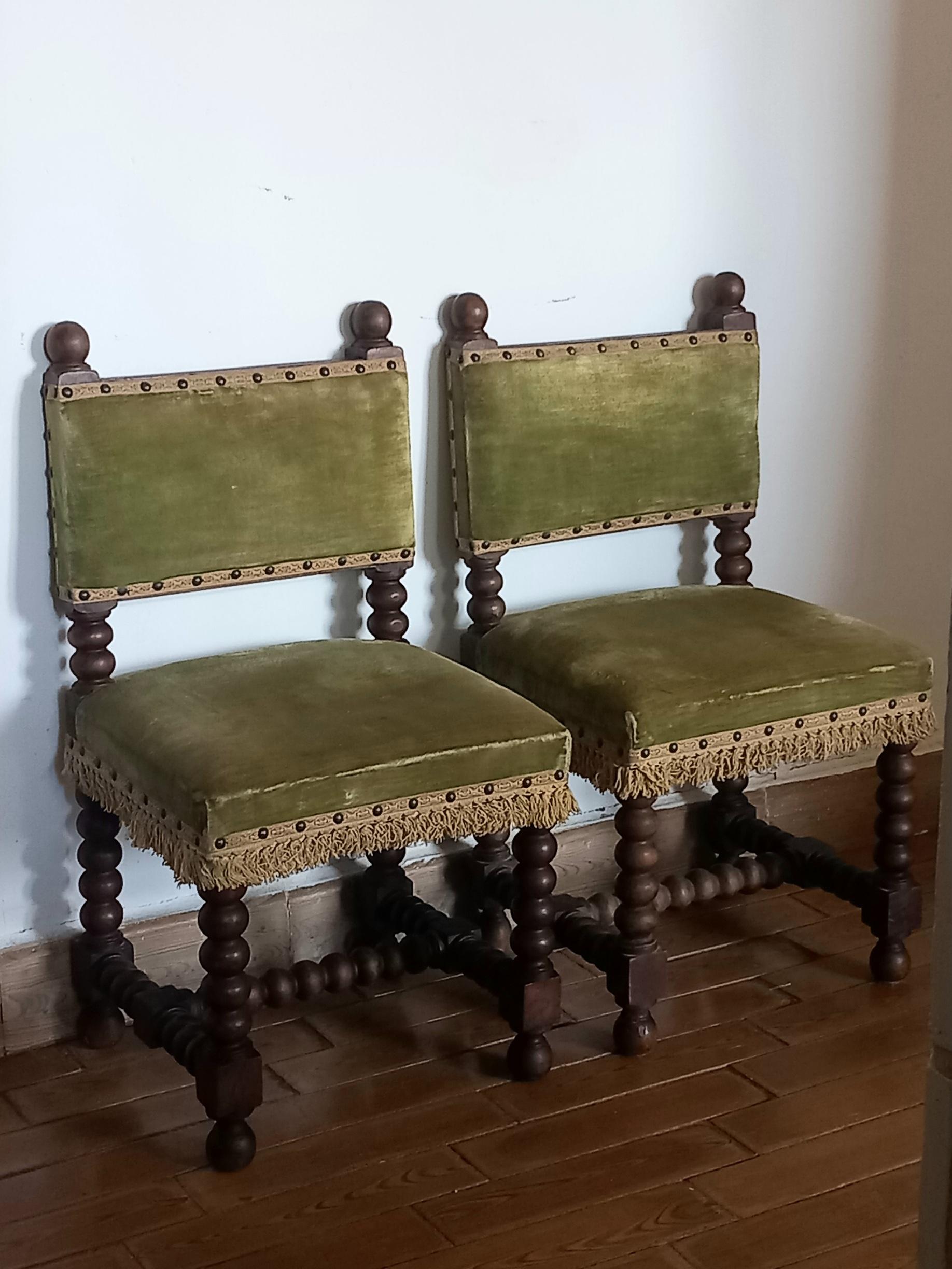 Pair of small chairs or stools with backrests and turned legs in the shape of a cabolla. They are made of fruit or oak wood and the seat and back are upholstered with green velvet topped with fringes and studs.
  They are two spectacular, precious
