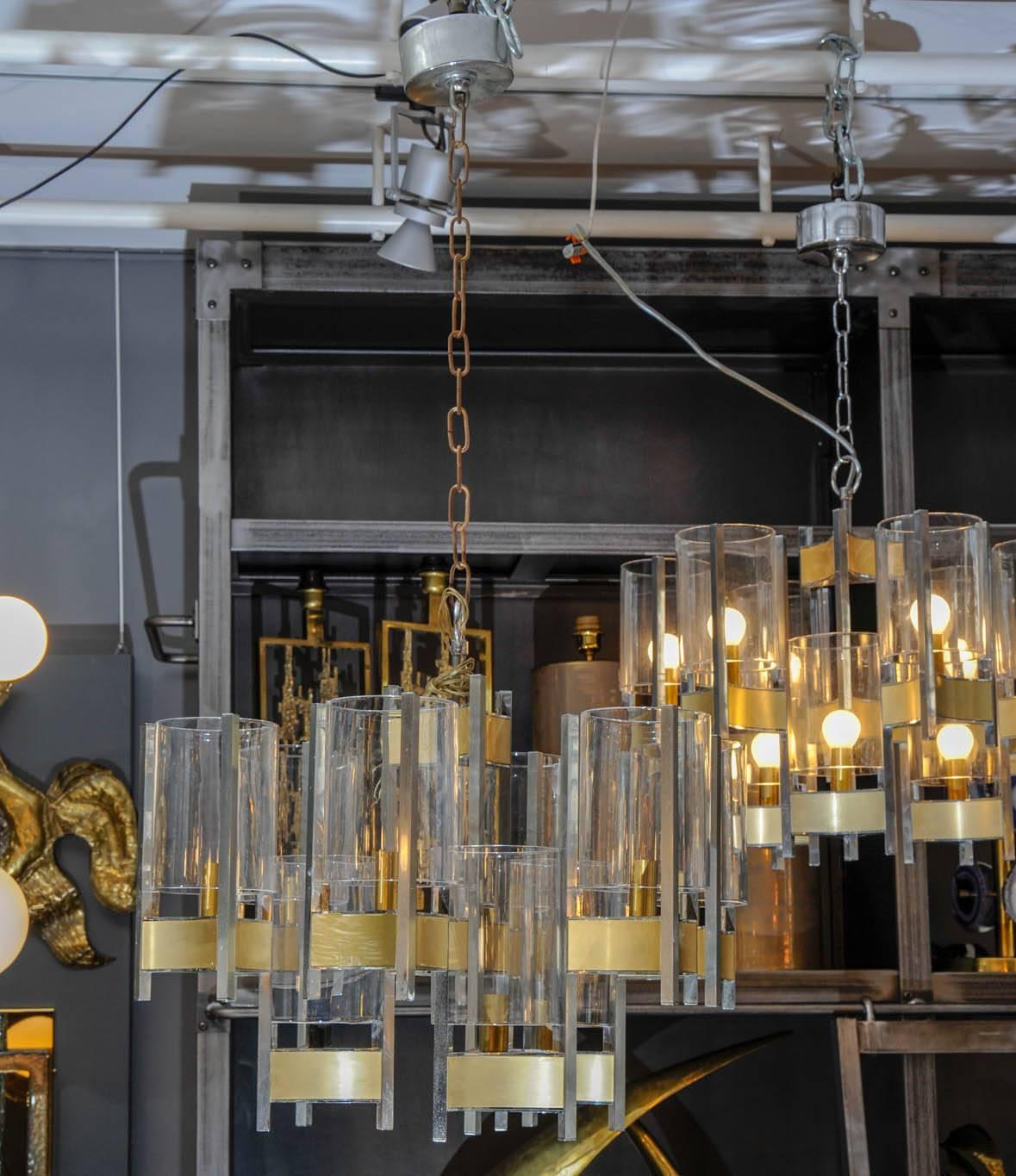 Pair of chandeliers designed by Sciolari with nine lights, made of nickel finish stems and brass color panels. Each arms support a clear glass cylinder shade.