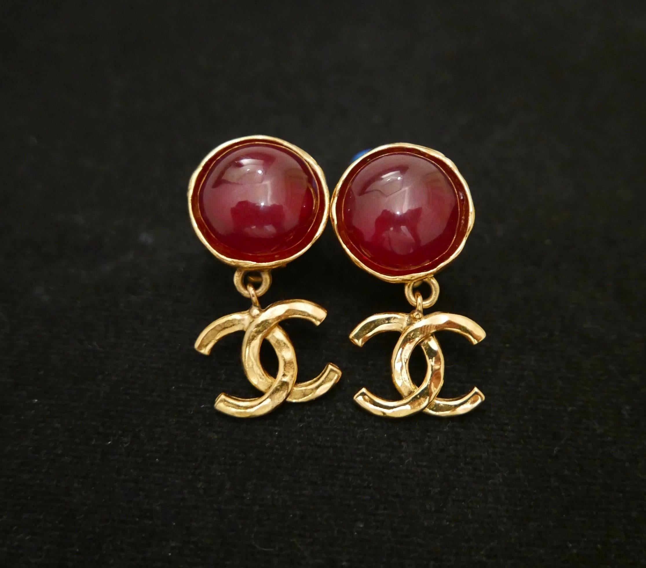 Pair of 1990s Chanel gold toned earclips featuring a red gripoix hemisphere adorned with a dangle gold toned CC logo. Measures approximately 4.4 x 2.2cm. Stamped Chanel 95P, made in France. Clip on style. Comes with box. 

Condition: Minor signs of