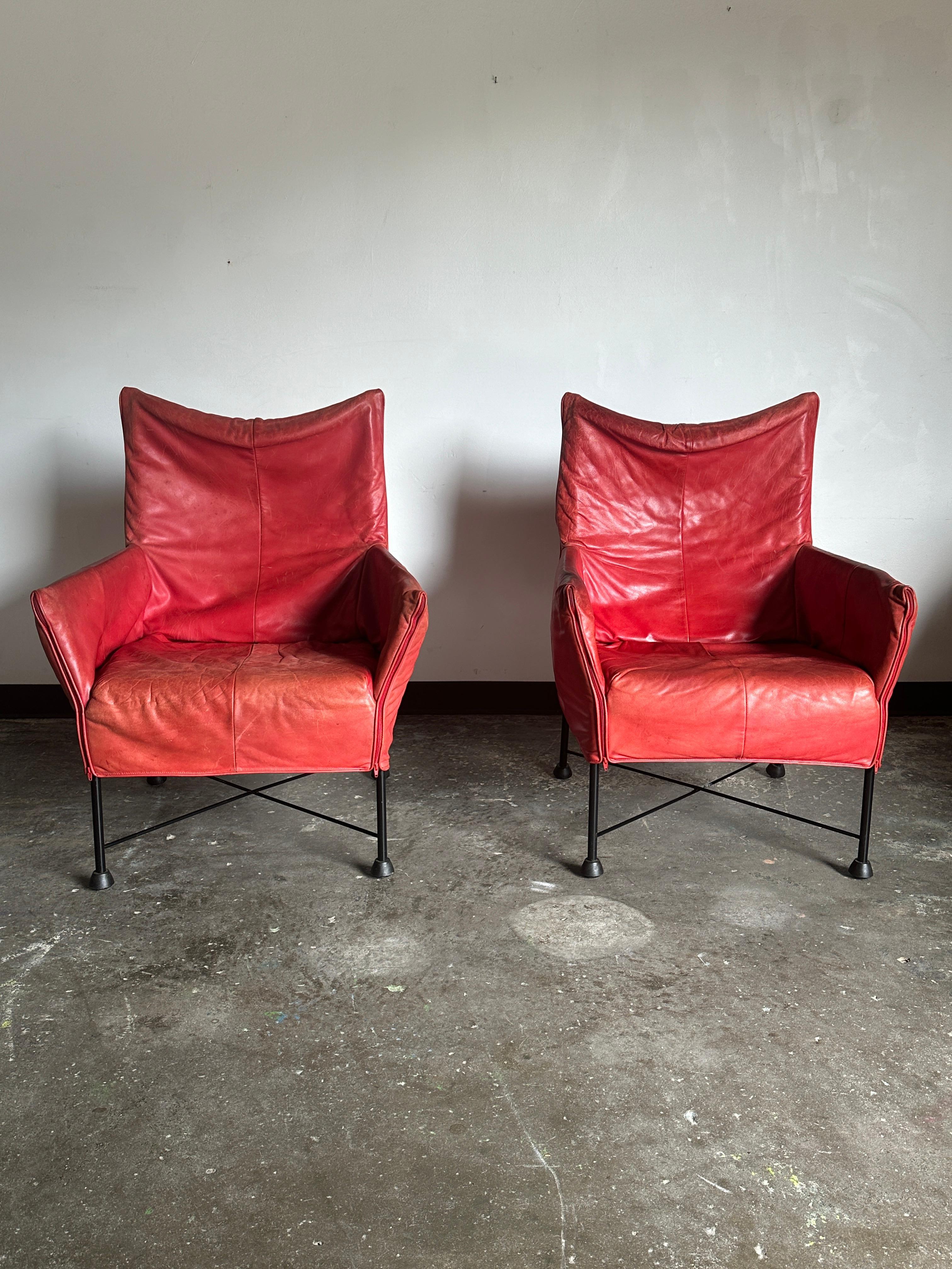 Pair of leather Chaplin dining armchairs in a patinaed red leather. Each chair has a zippered cover over a black frame. Chairs can be used for dining, lounging, or in any way that you should desire. Each chair does have age-consistent wear with