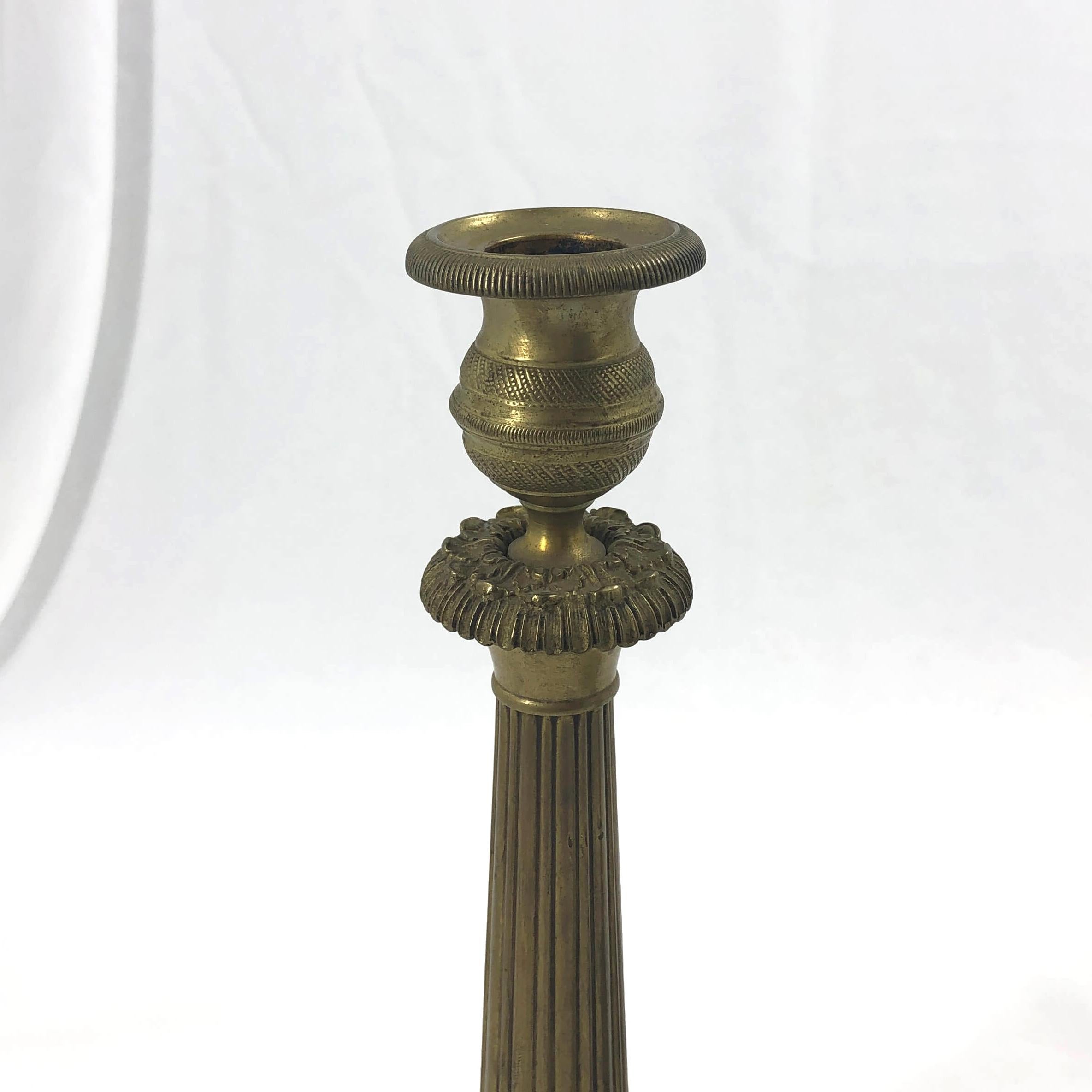 Pair of French Charles X brass candlesticks with chased cups, floral motifs, a reeded tapered shaft on a floral relief base.
  