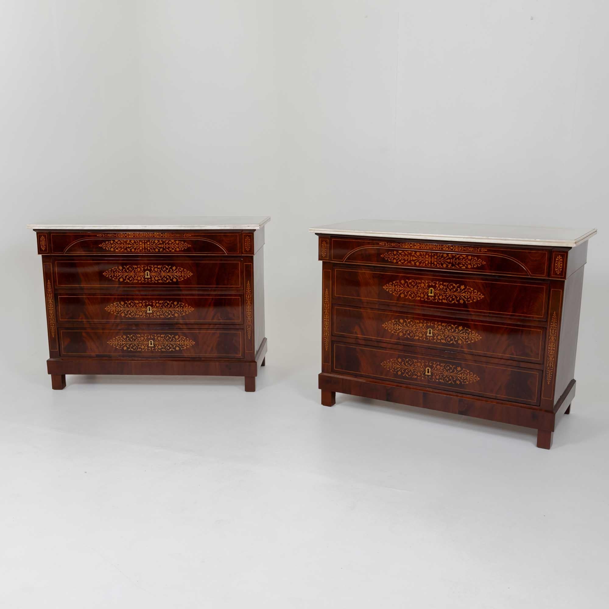 Pair of Charles X chests of drawers in mahogany veneer with white profiled marble tops and fine maple inlays on the front of the drawers as well as the pilasters. The chests are fitted with four drawers, the top drawer being slightly different in