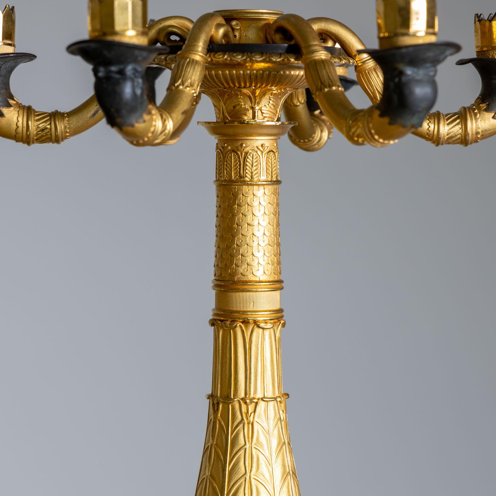 Pair of Charles X candlesticks with six arms on marble pedestals. The candlesticks are made of partly gilded bronze and decorated with nymphs, lion paws and lion masks, among other things. The final crowning is missing, but at a height of 75 cm they