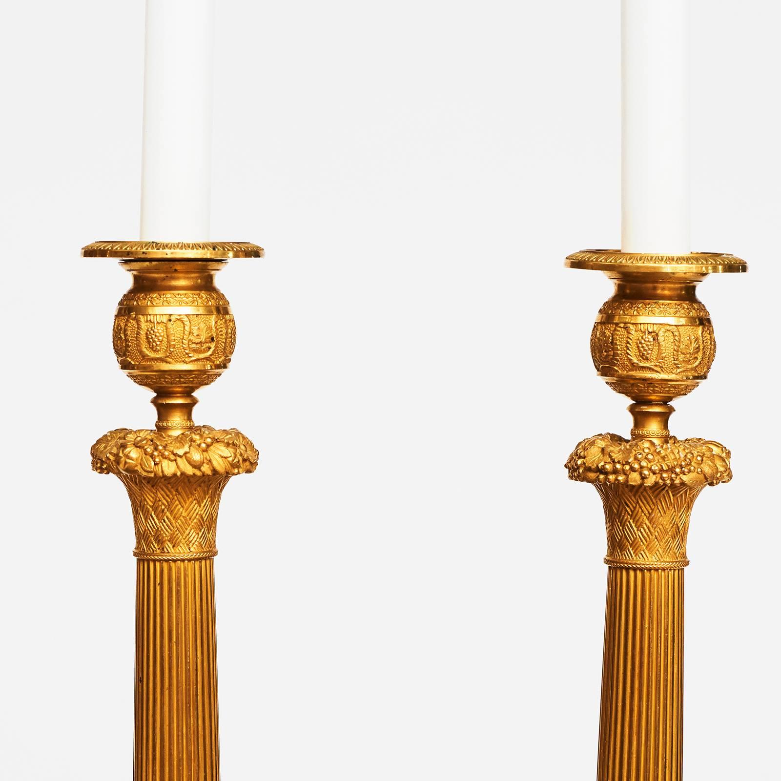 A good pair of French Charles X ormolu candlesticks, circa 1820s, with inset bobèches above a Campana vase, a cast fruit band and a spreading tapered stem, the round base with cast palmette and acanthus leaf decoration.

 