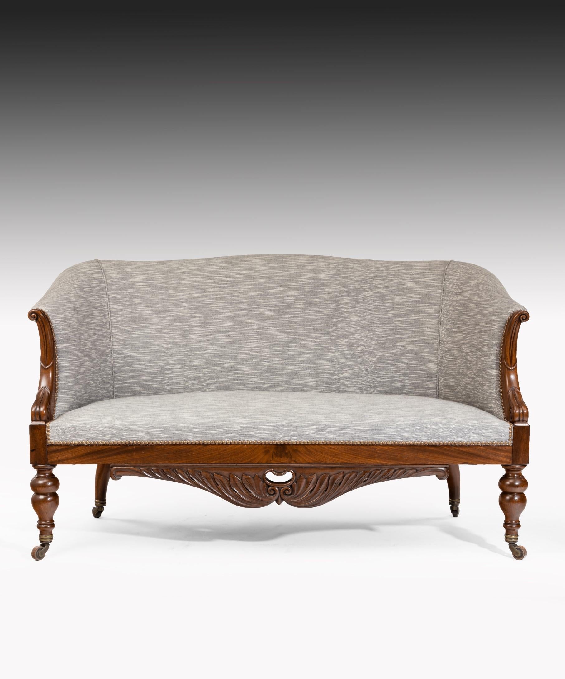 A comfortable pair of Charles X sofas with carved mahogany showwood frames; the sofa's upholstered back and seat with scrolling mahogany arms and a seat rail veneered and carved in well figured mahogany. The sofa is raised on turned front legs and