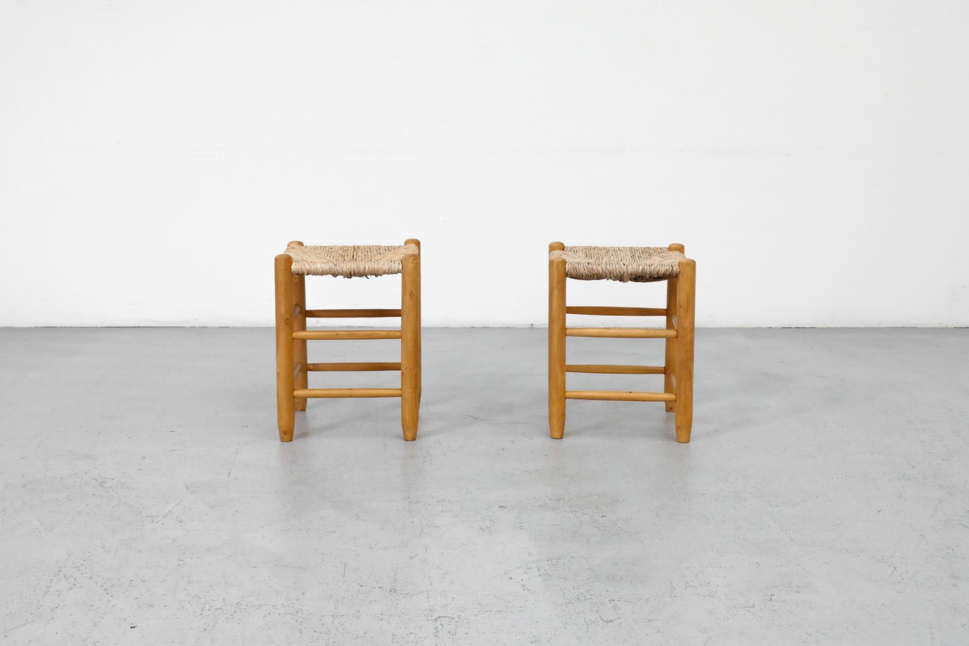 Pair of Charlotte Perriand style dining height stools with hand-woven rush seats and beautifully aged oak frames. These stools are in original condition with visible wear and may have some rush breakage. Wear is consistent with their age and use.