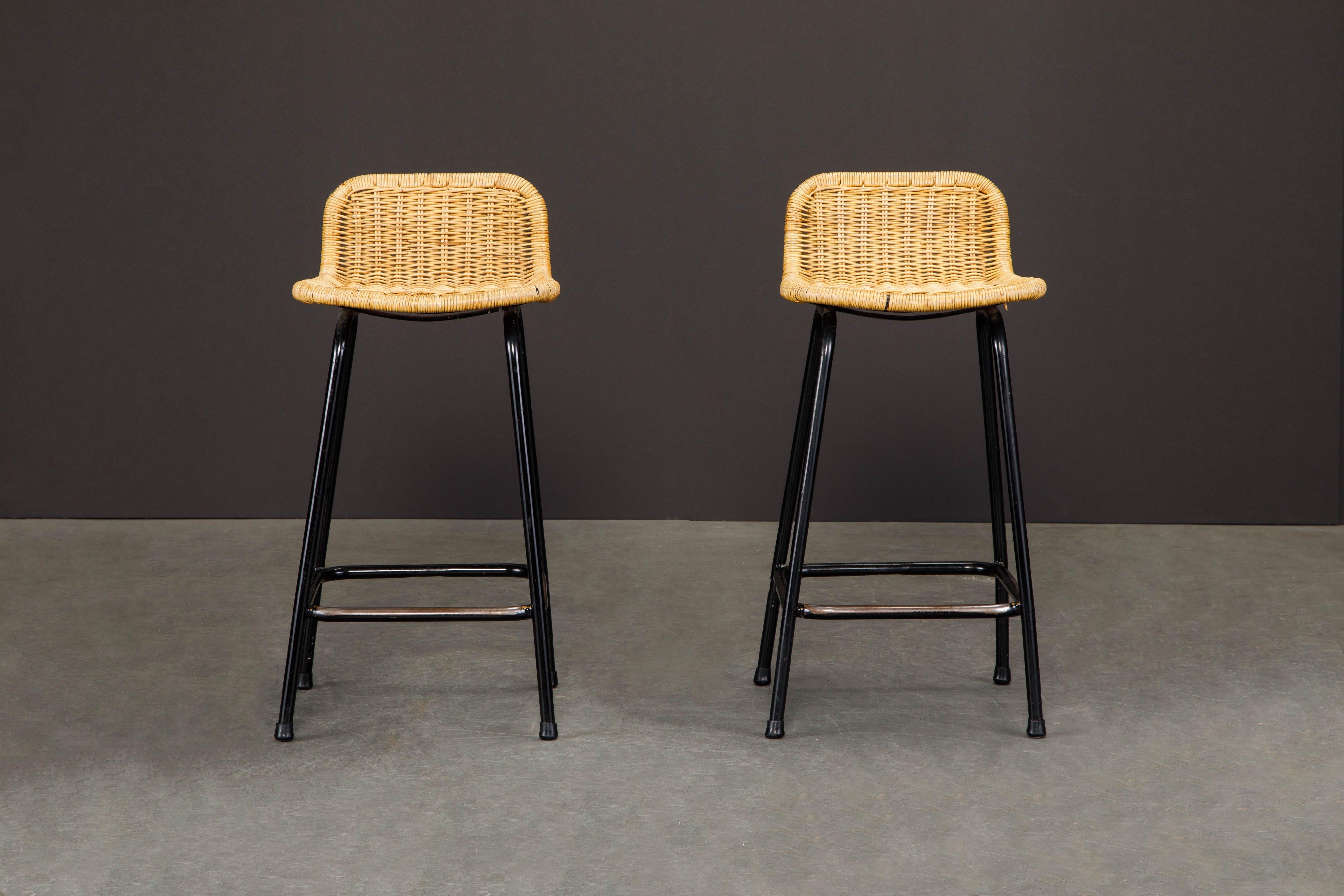 A beautiful pair of Charlotte Perriand style bar stools with low square rattan seats on black enameled tubular frames in original condition with light wear and patina. Seat height measures 24