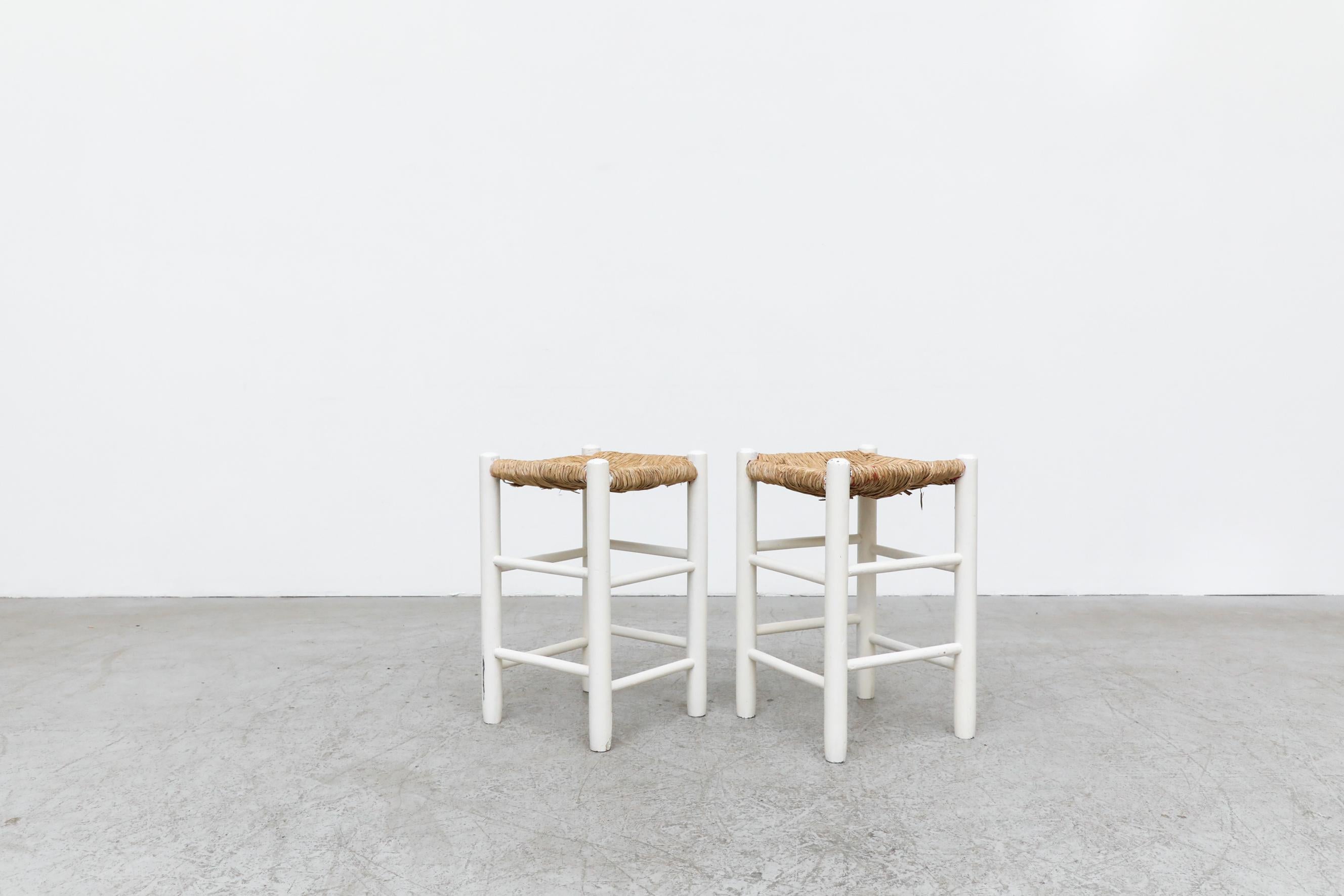 Paire de tabourets carrés de style Charlotte Perriand avec assise en jonc tissé et structure peinte en blanc. En état d'origine, avec une usure visible et des rayures correspondant à leur âge et à leur utilisation. D'autres tabourets similaires sont