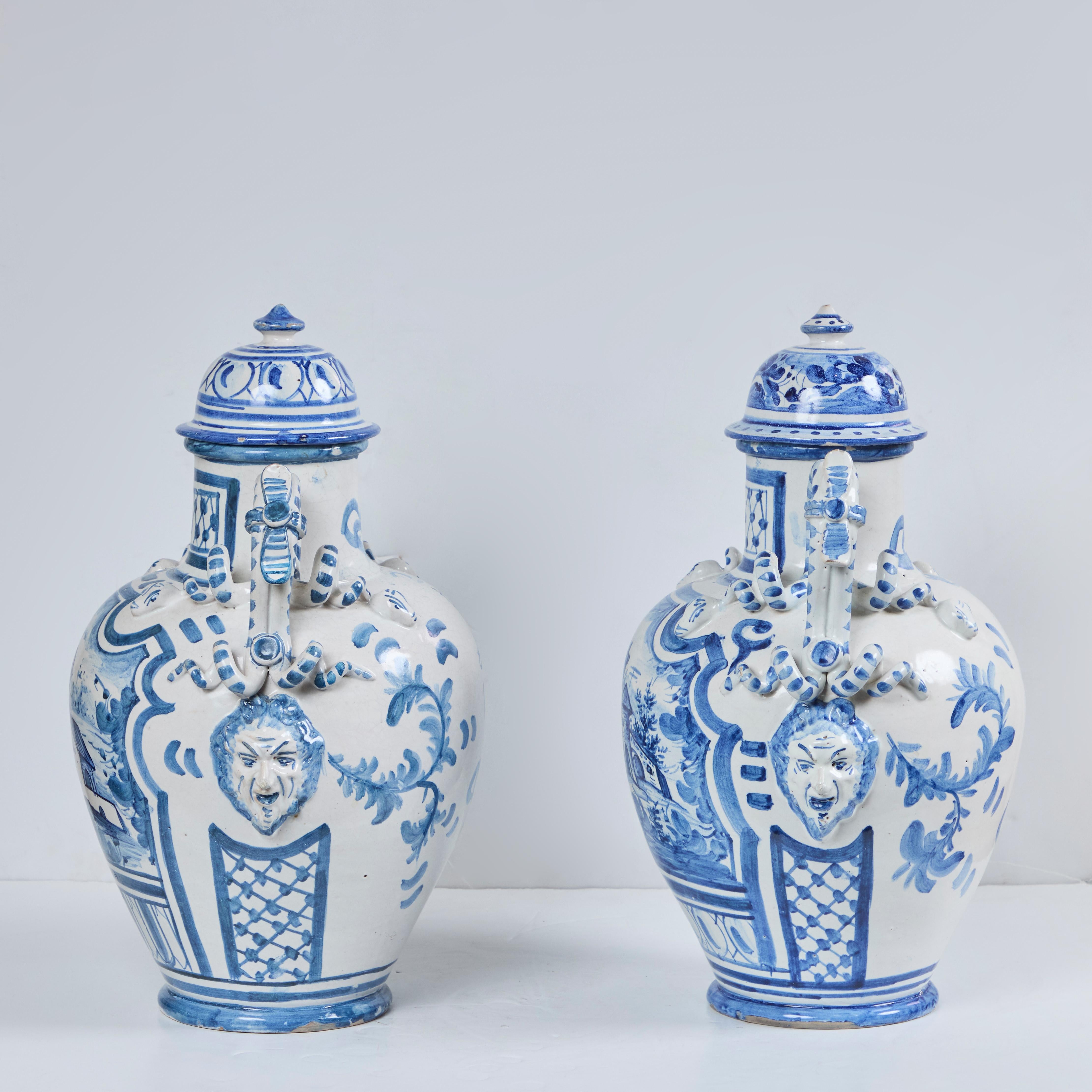 Encantadora pareja de jarras de loza recubiertas con asas de serpiente, edificios de pueblo y caras figuradas en los laterales.