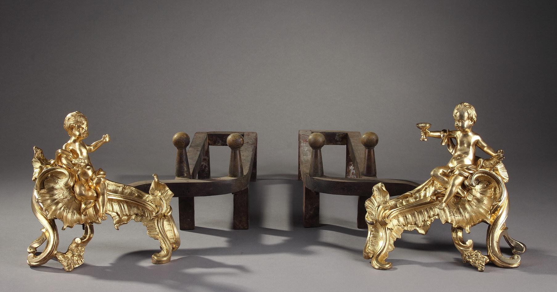 Pair of chased and gilded bronze andirons, each adorned with a putto girded with a drapery, seated on a moving base, carved with gadrooned foliage. One of the putti is holding a cup towards the second one who is holding a flower. Louis XV period.