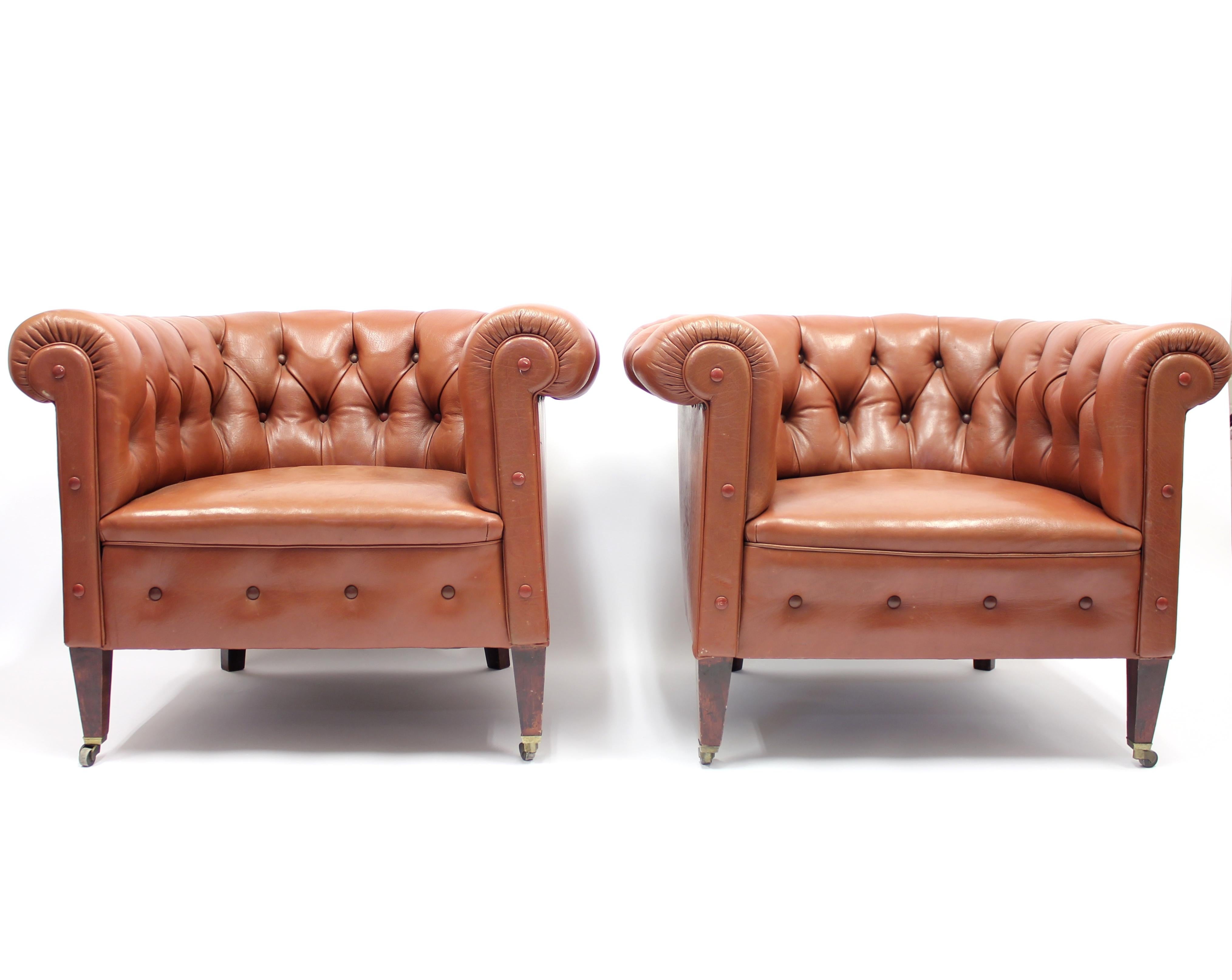 Pair of 1930s-1940s Chesterfield club chairs in brown leather on mahogany legs with brass castors on the fornt legs. Unusual and superb shape. The leather may be of a later date but has some age to it. Very good condition when age is considered with