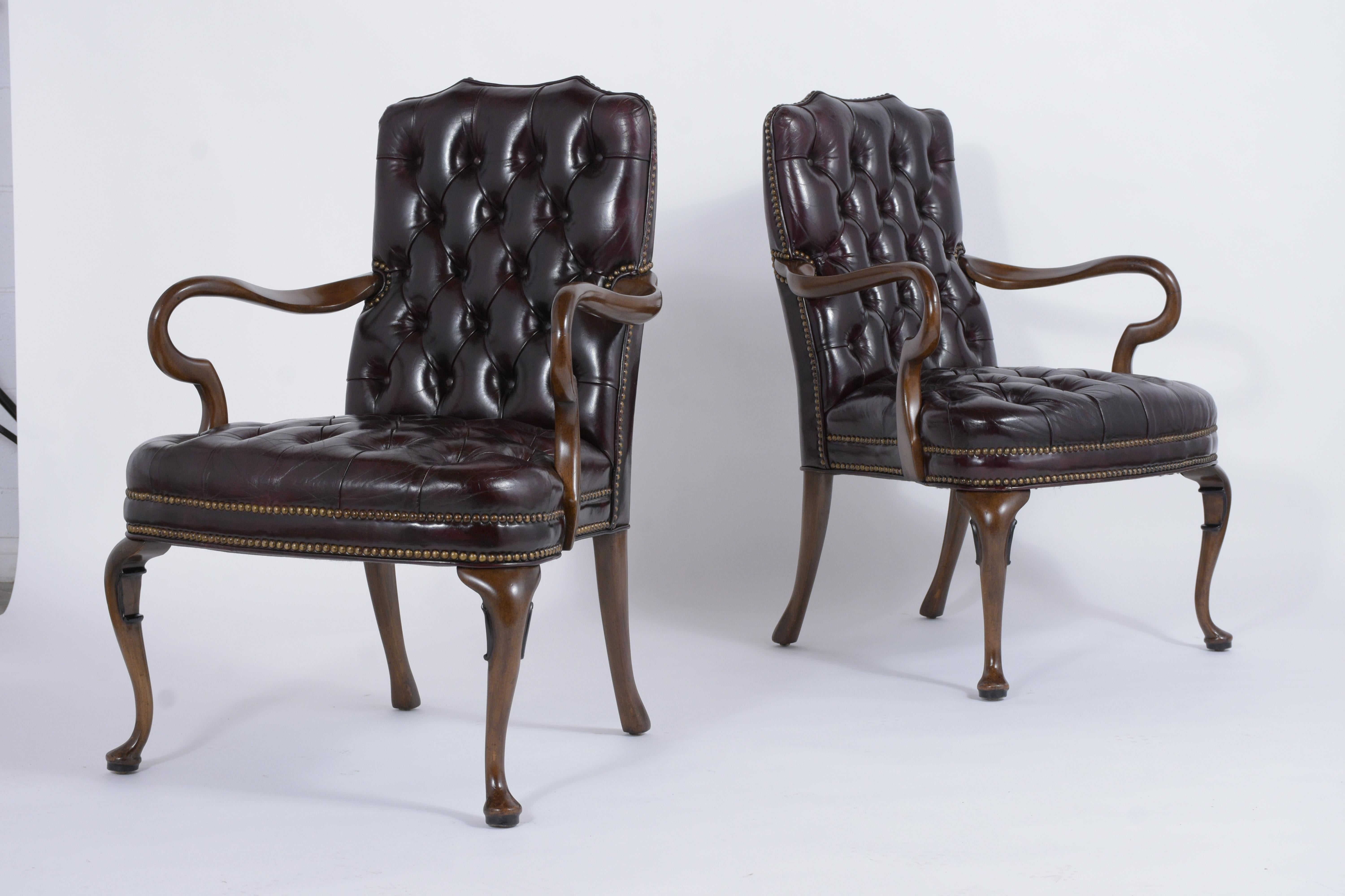 A pair of 1950s Chesterfield style office chairs crafted out of mahogany wood finished in a dark walnut color with a newly lacquered finish and are completely restored. These armchairs are upholstered in their original tufted leather, have been