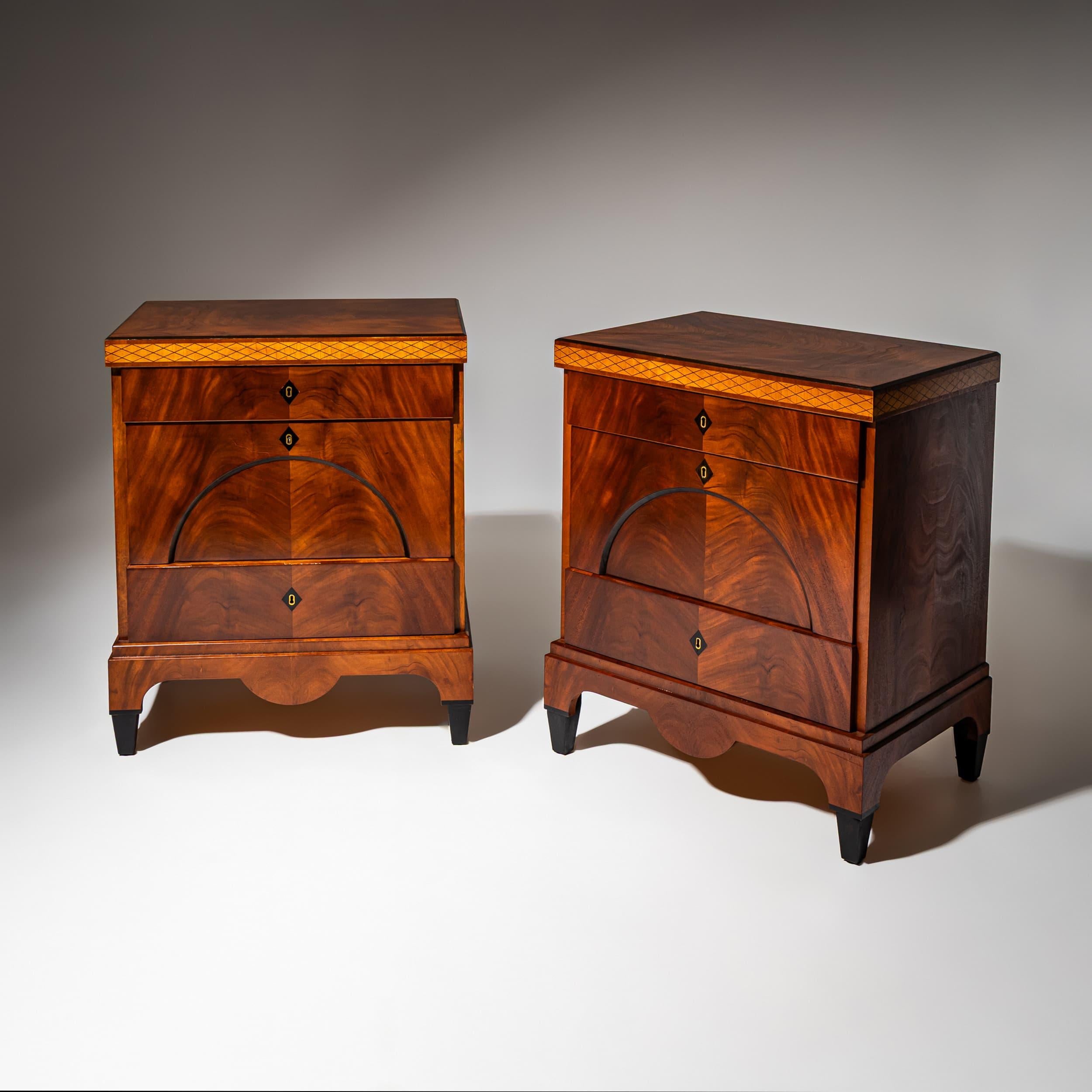 Paire de commodes à trois tiroirs chacune dans le style Biedermeier. Reposant sur des pieds ébonisés, les coffrets présentent un tablier profondément incurvé. Le tiroir central est conçu avec un arc segmentaire, et les entrées de clé en forme de