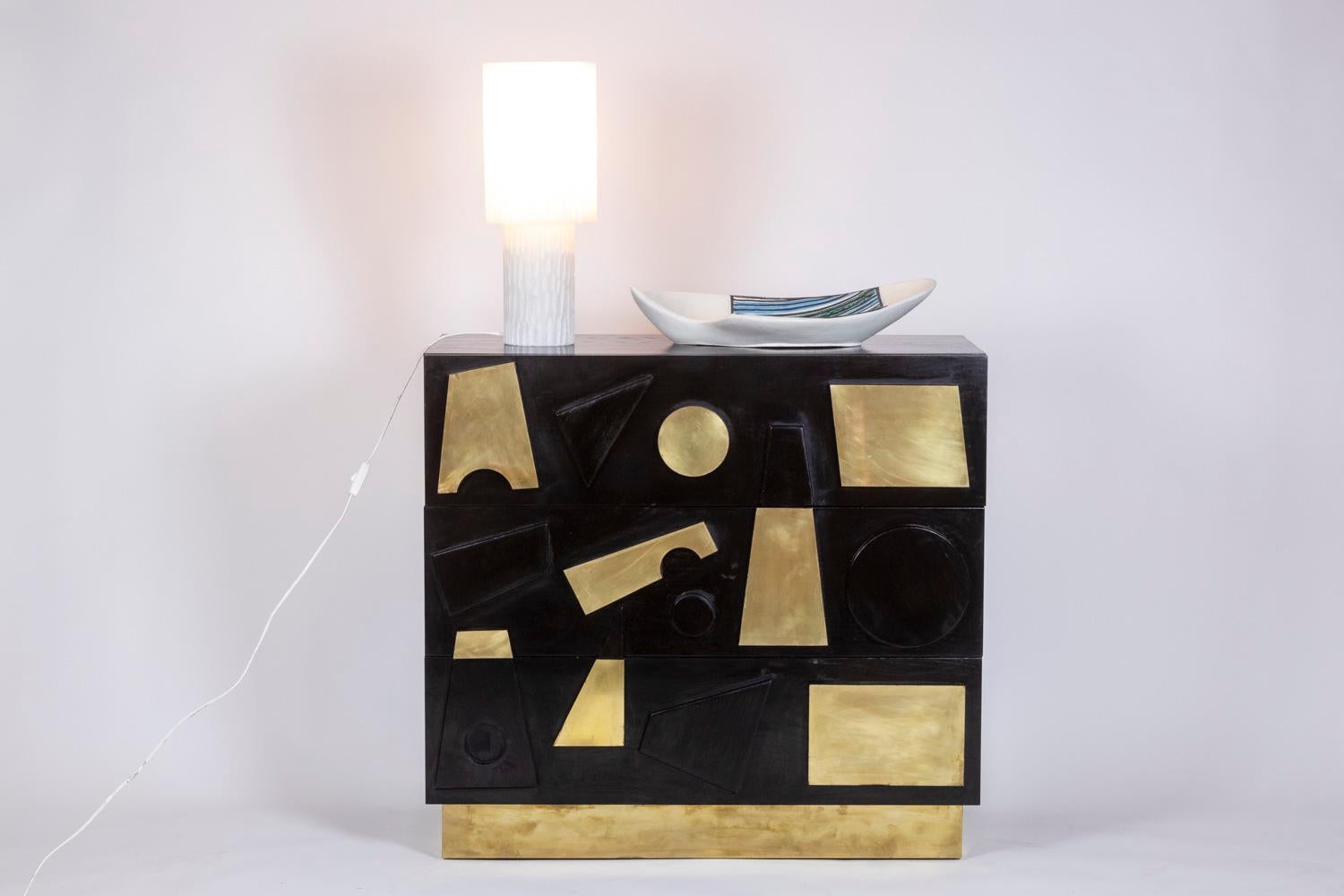Pair of chests of drawers in a rectangular shape, each chest of drawers opening on the front with three drawers, in black lacquered beech decorated with geometric shapes, some in black lacquer and others in gilded brass. Base in gilded brass in a