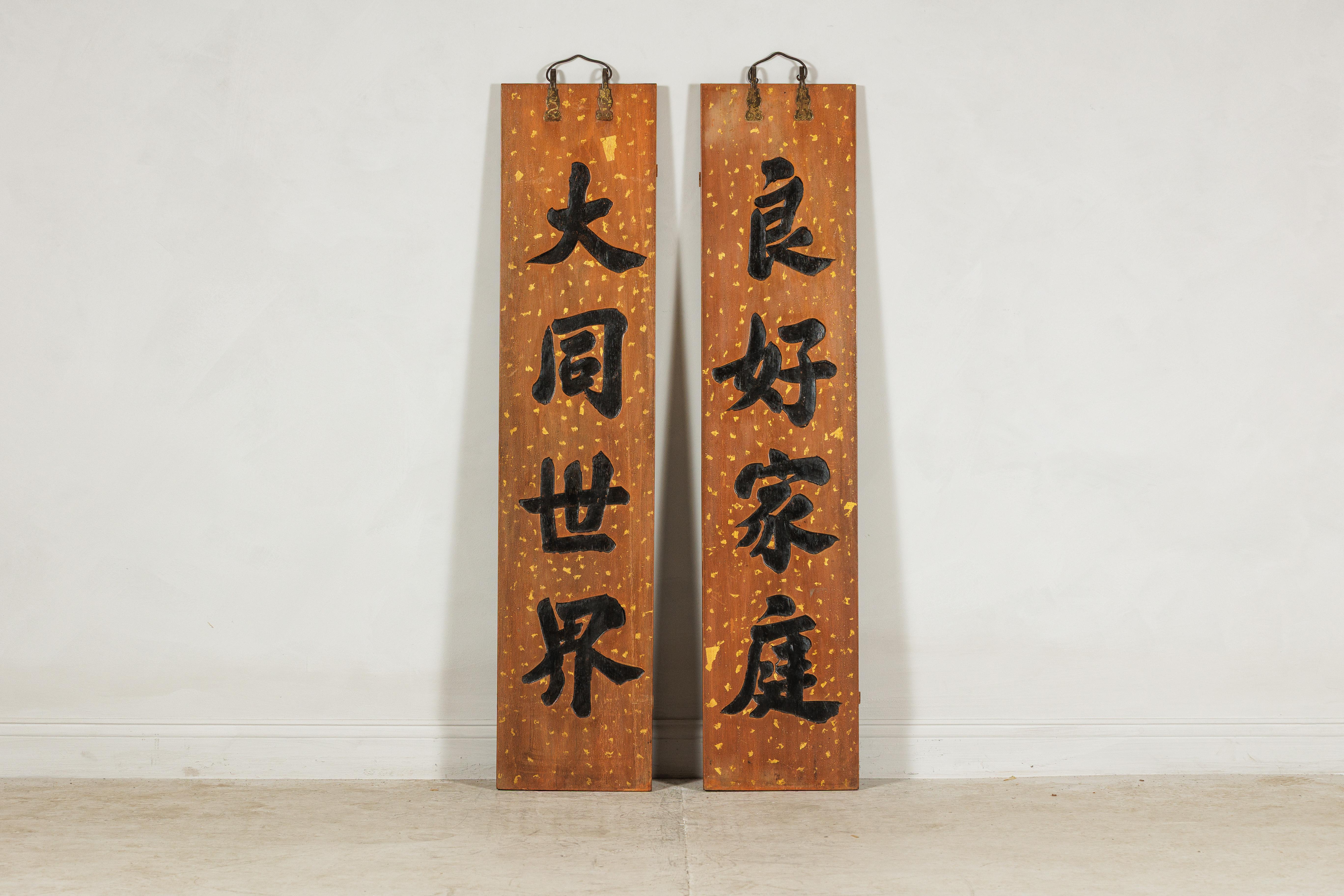 Este par de letreros chinos verticales, de principios del siglo XX, está ricamente decorado con una atrevida caligrafía tallada a mano. Cada panel está hecho de madera y acabado en un cálido fondo lacado, acentuado con motas doradas dispersas que