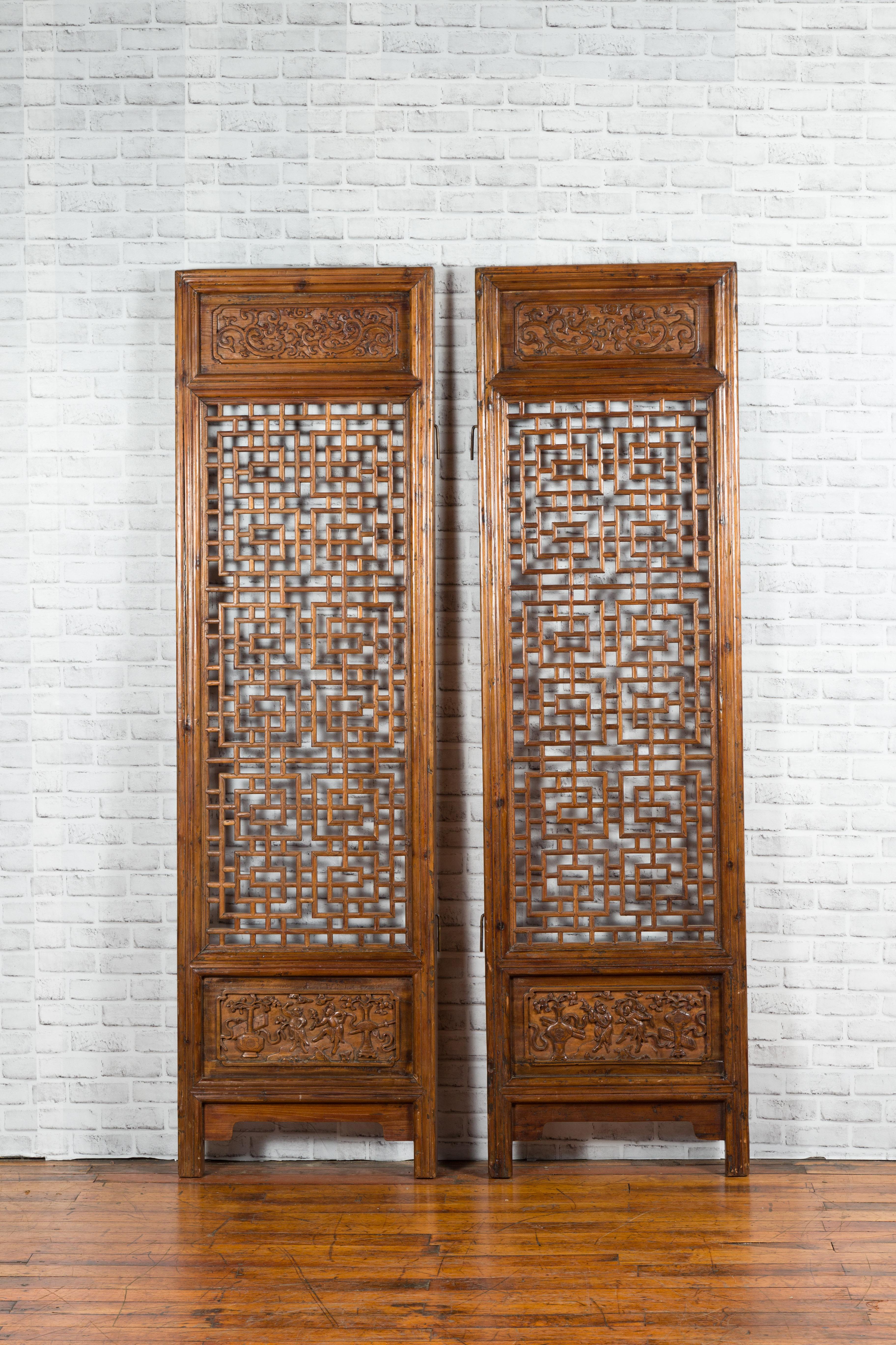 A pair of Chinese antique carved screens from the 19th century, with fretwork motifs and low-relief panels. Created in China, each of this pair of wooden screens attracts our attention with their fretwork design surrounded by carved panels. The