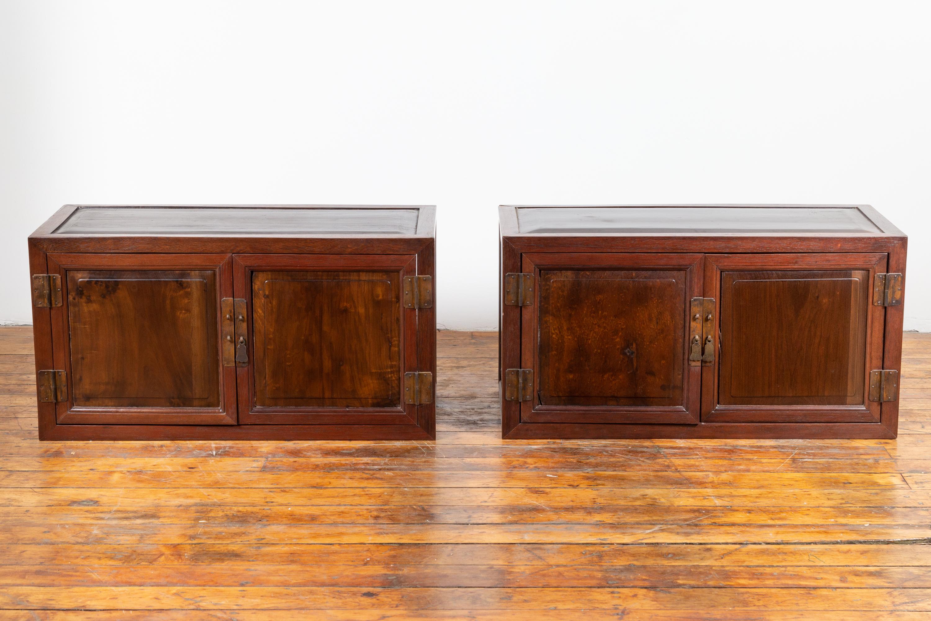 A pair of antique Chinese wooden low cabinets from the early 20th century, with brass hardware. Born in China during the early years of the 20th century, each of this pair of wooden buffets features a rectangular top with slightly raised central