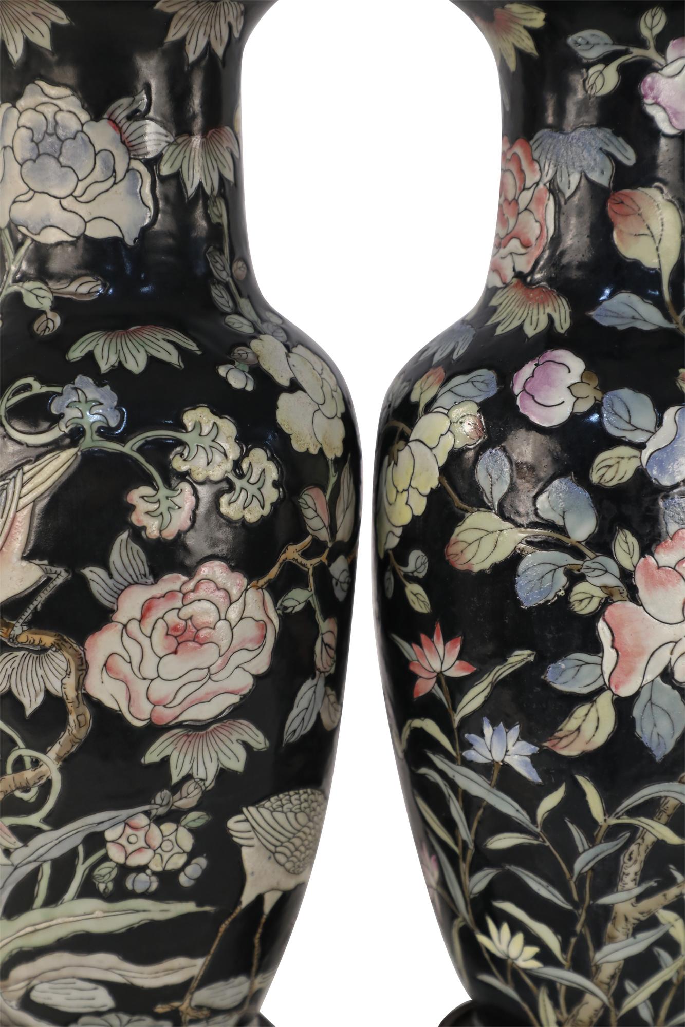 Pair of Chinese black ceramic table lamps made from baluster-shaped vases decorated with birds amid blooming florals in pinks, yellows and blues, and wooden bases.