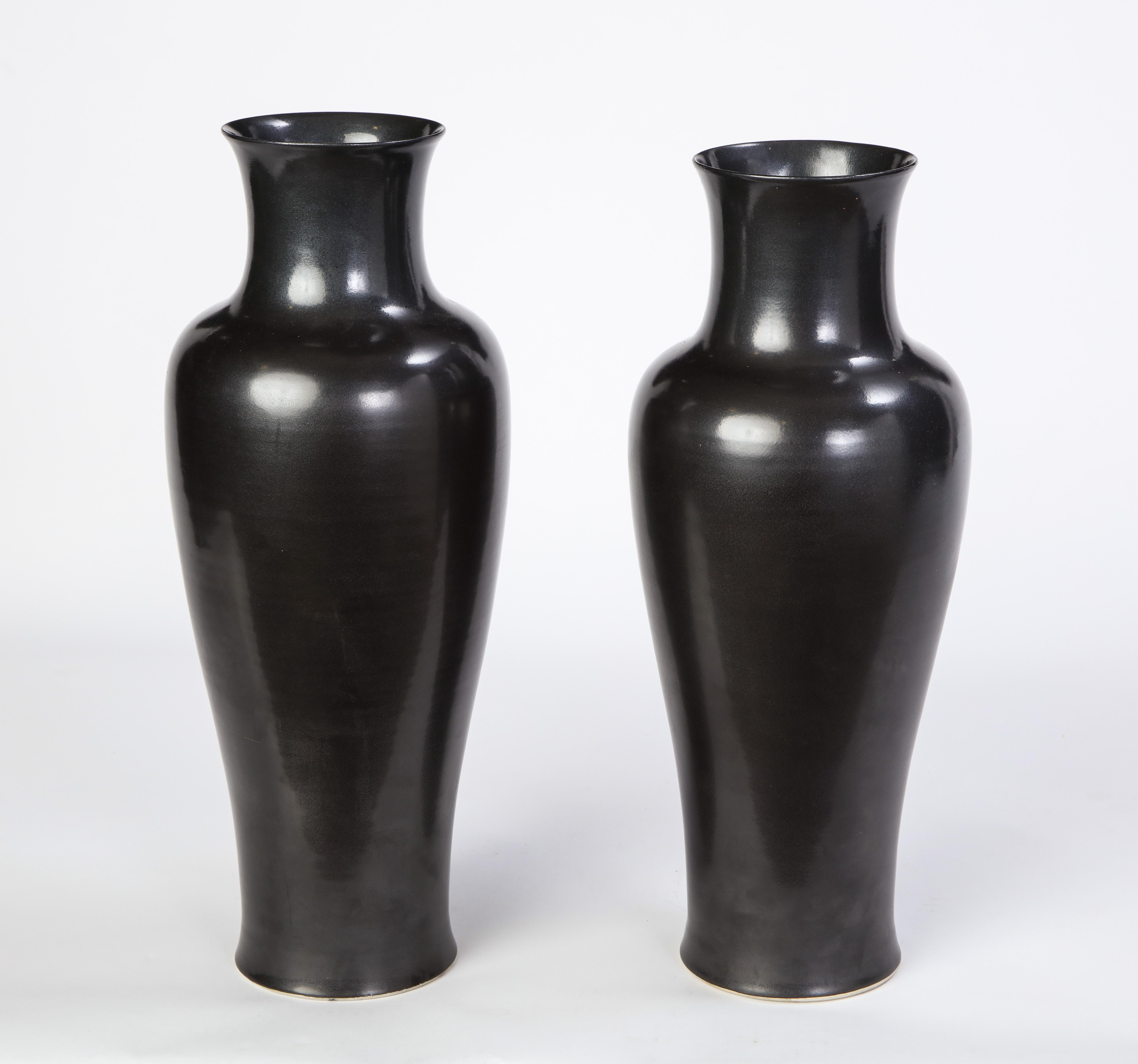 A striking pair of modern, black-glazed Chinese vases, perfect for accenting contemporary or traditional interiors by adding a moody element to a side table or credenza vignette. The sleek curvature of each vase provides elegance while the glaze