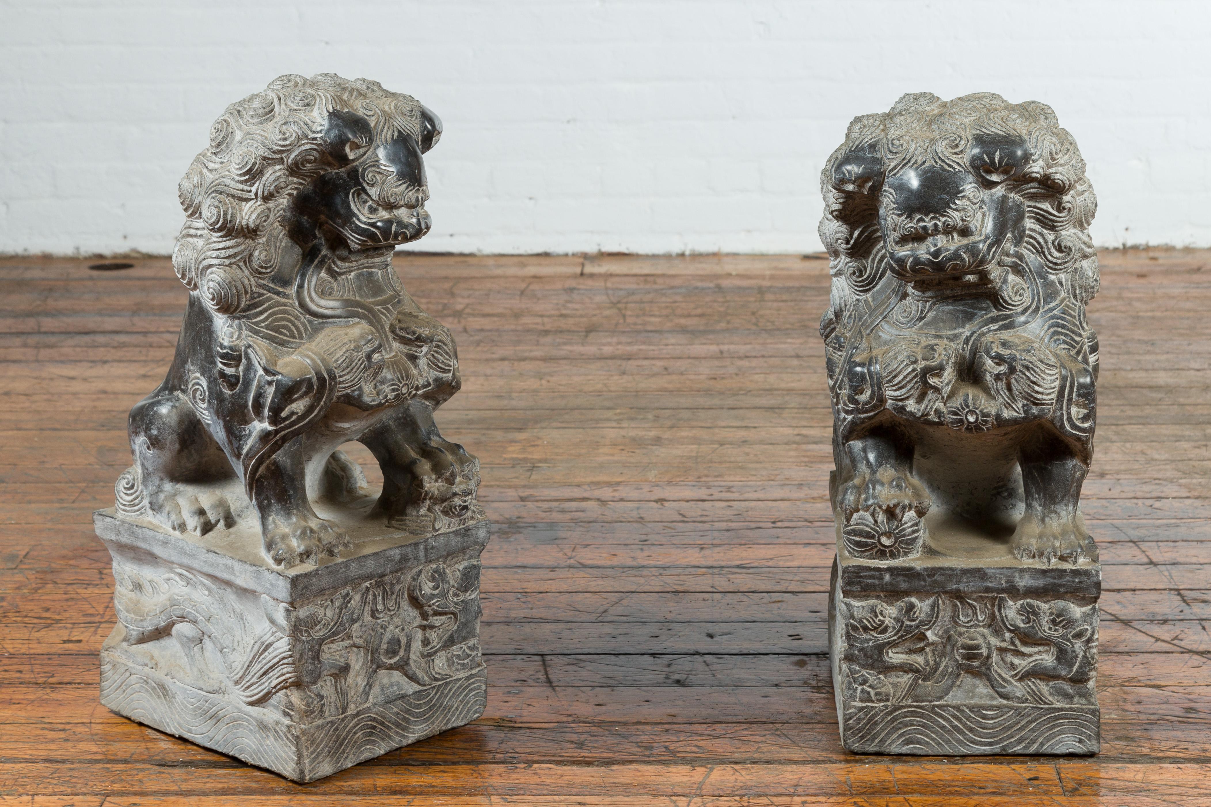 A pair of contemporary Chinese black marble left and right facing foo dogs guardian lions on rectangular bases. Created in China during the 21st century, this pair of black marble guardian lions features a left and right facing male and a female,